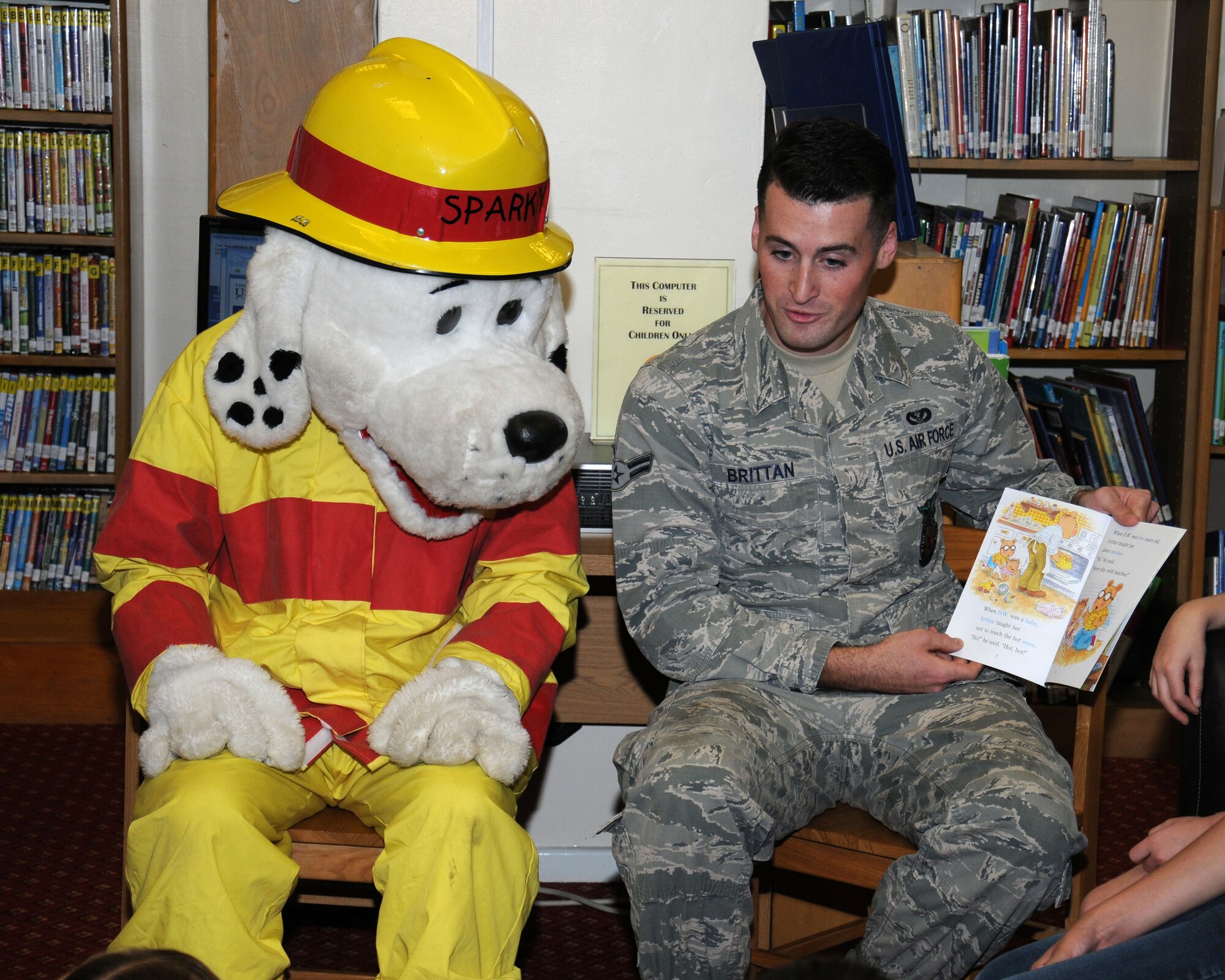 U.S. Air Force Airman 1st Class Kevin Brittan, right, 100th Civil Engineer Squadron Fire Department firefighter from Lindenhurst, N.Y., and “Sparky,” 100th CES Fire Department mascot, read a book to Team Mildenhall children Aug. 21, 2013, at the library on RAF Mildenhall, England. The 100th CES Fire Department firefighters read at the library twice a year and once a year at the Child Development Center. The aim is to make children aware of the dangers of fire and ways to prevent them. (U.S. Air Force photo by Gina Randall/Released)