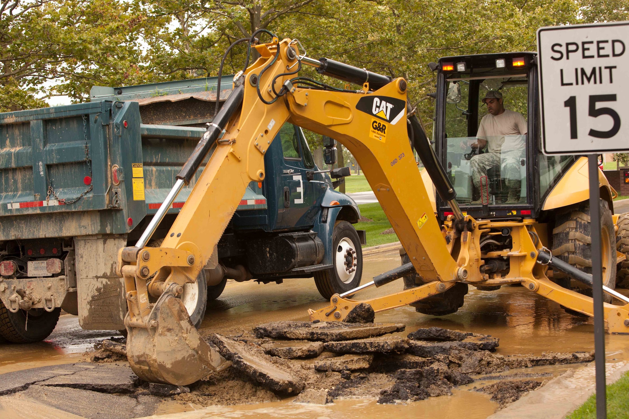 Staff Sgt. Corey Kautner, 87th Civil Engineer Squadron heavy equipment operator, uses a backhoe to remove part of an asphalt road to get to a broken water main Aug. 9, 2013, just inside the McGuire Main Gate on Joint Base McGuire-Dix-Lakehurst, N.J. The water main caused major damage and flooding to the roads, which temporarily closed the gate’s inbound lanes. Kautner hails from Chicago. (U.S. Air Force photo by Wayne Russell/Released)