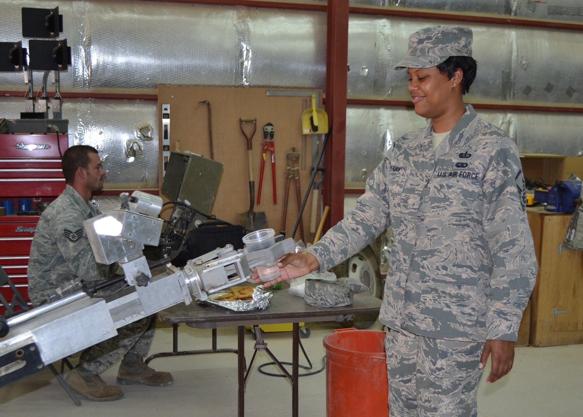 Staff Sgt. Levi Owen maneuvers an explosive ordinance disposal robot to hand Master Sgt. Latoya Perry a cup at the 64th Air Expeditionary Group in Southwest Asia, July 26, 2013. Owen is a 64th Expeditionary Support Squadron civil engineer electrical power production craftsman deployed from Aviano Air Base, Italy, and hails from Liberty, S.C. Perry is a 64th ESS services flight chief deployed from Joint Base Langley-Eustis, Va., and hails from Fayetteville, N.C. (U.S Air Force photo/Staff Sgt. Minerva H. Rosario)