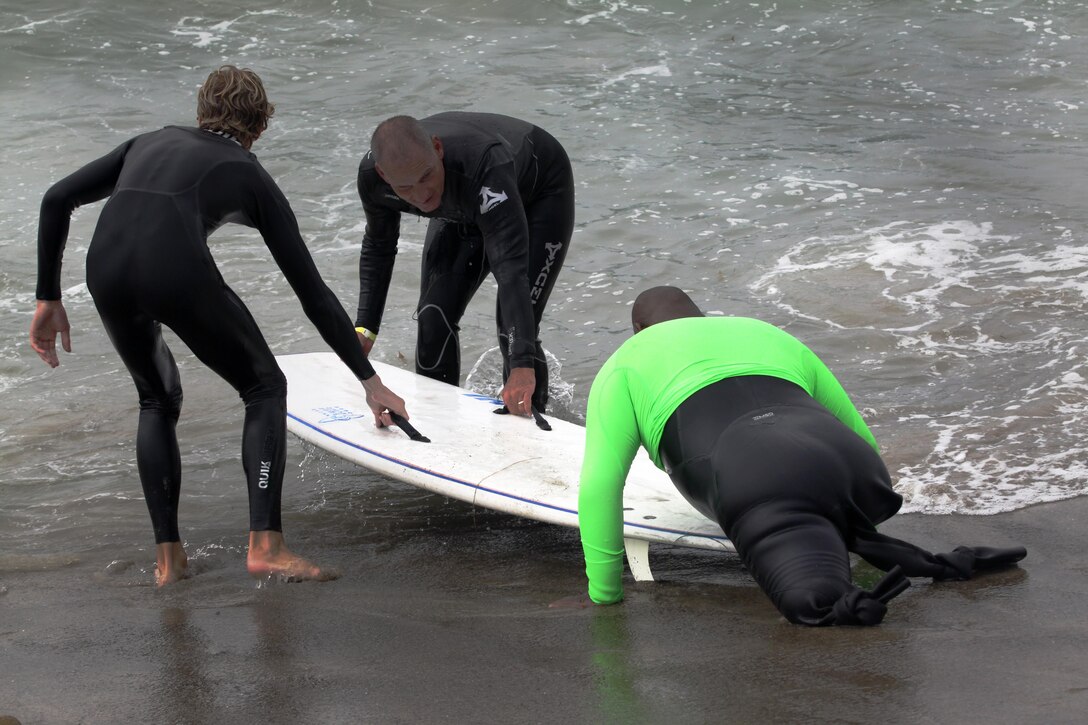 Two surf instructors assist Cpl. Toran Gaal, a double amputee, onto his surfboard to catch another wave during the Operation Amped surf clinic at San Onofre beach here, Aug. 24. During the three days, veterans are paired with a surf instructor to teach them the fundamentals of surfing.