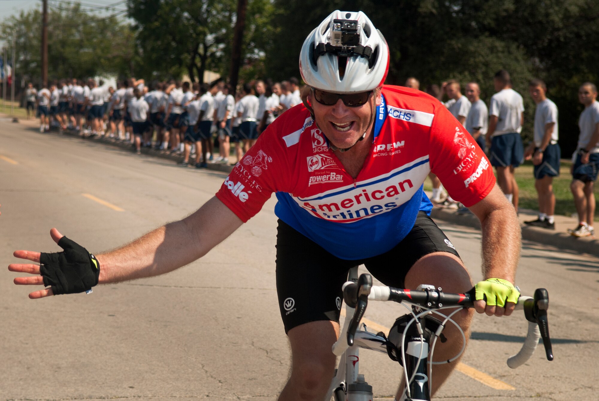 A Hotter'N Hell Hundred rider greets Airmen in training at Sheppard Air Force Base, Texas, on his way out of the base Aug. 24, 2013. After "Airpower Alley" and a rest stop, bicycle riders rode through a gauntlet of hundreds of Airmen screaming and cheering them on to the finish line. As part of the event, hundreds of Sheppard volunteers helped riders needing a break at the last rest stop before the finish line. The annual race is in its 32 year and celebrates the founding members of Texoma with a 100-mile race in 100-degree temperatures. (U.S. Air Force photo/Staff Sgt. Mike Meares)