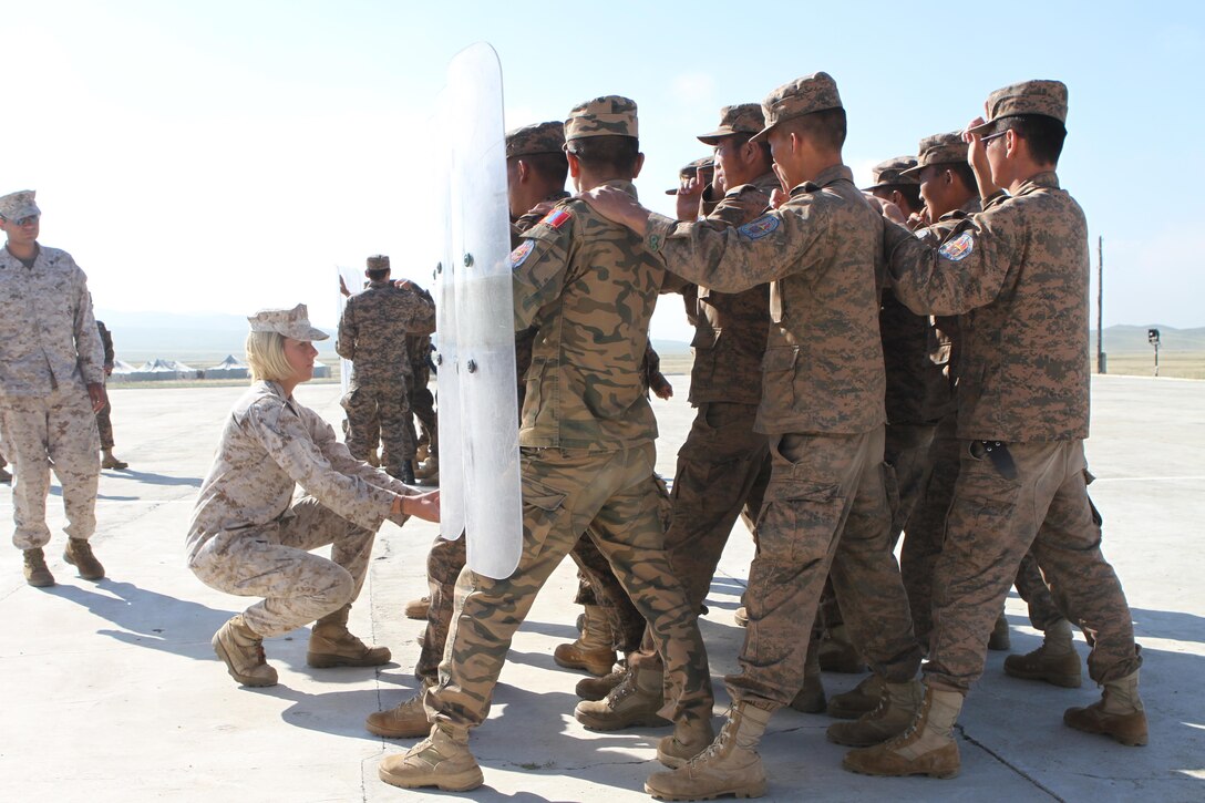 U.S. Marine Lance Cpl. Kayla Piatt  with 3rd Law Enforcement Battalion, III Marine Expeditionary Force, adjusts the shields of Mongolian Armed Forces service members as they practice riot control techniques during the  Non-Lethal Weapons Executive Seminar (NOLES) in Five Hills Training Area, Mongolia, August 24, 2013. NOLES is a regularly scheduled field training exercise and leadership seminar sponsored annually by U.S. Marine Corps Forces Pacific, and it is designed to promote awareness and effective use of non-lethal weapons as a tool to maintain order in low-intensity or civil unrest situations.
