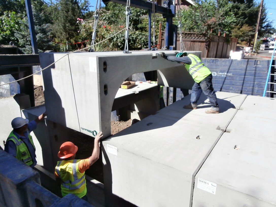 Workers place a precast arch culvert section at S.E. Tacoma Street at 21st Avenue, replacing the existing small culvert with a larger, natural-bottom culvert. The Corps and the Portland Bureau of Environmental Services are restoring a portion of Crystal Springs Creek to improve fish habitat and passage.  The new culvert is a key element of the restoration effort.