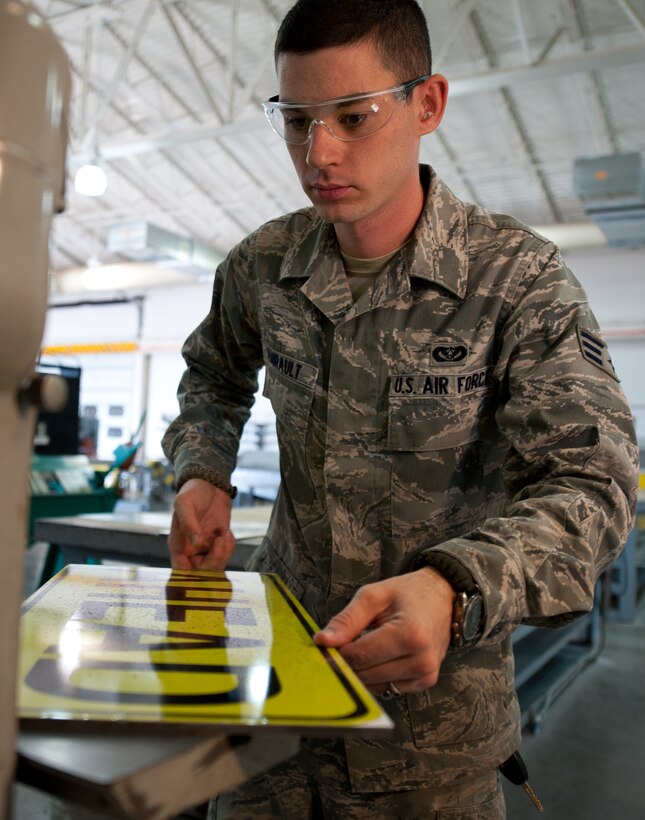 Senior Airman Benjamin Amirault, 28th Civil Engineer Squadron structures technician, uses a belt sander to round the corners of a traffic sign at Ellsworth Air Force Base, S.D., Aug. 15, 2013. Technicians flatten the corners of each sign to provide a finished product free of sharp edges. (U.S. Air Force photo by Airman 1st Class Alystria Maurer/Released)