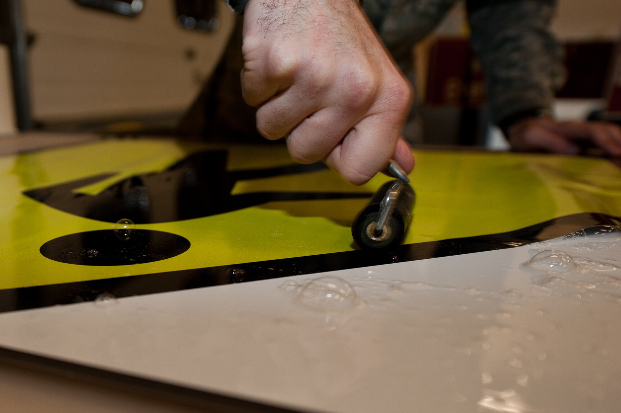 Senior Airman Benjamin Amirault, 28th Civil Engineer Squadron structures technician, uses a roller to push out soap and water while constructing a crosswalk sign at Ellsworth Air Force Base, S.D., Aug. 15, 2013. This process eliminates air bubbles to ensure the sign properly adheres to the metal. (U.S. Air Force photo by Airman 1st Class Alystria Maurer/Released)