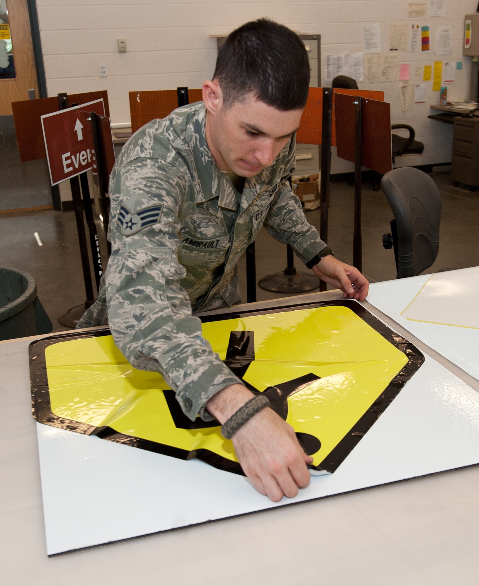 Senior Airman Benjamin Amirault, 28th Civil Engineer Squadron structures technician, lays out a crosswalk sign onto poly-metal backing at the sign shop at Ellsworth Air Force Base, S.D., Aug. 15, 2013. Amirault sprays rapid tac adhesion promoter and water-based solution on the metal prior to laying out the sign. (U.S. Air Force photo by Airman 1st Class Alystria Maurer/Released)