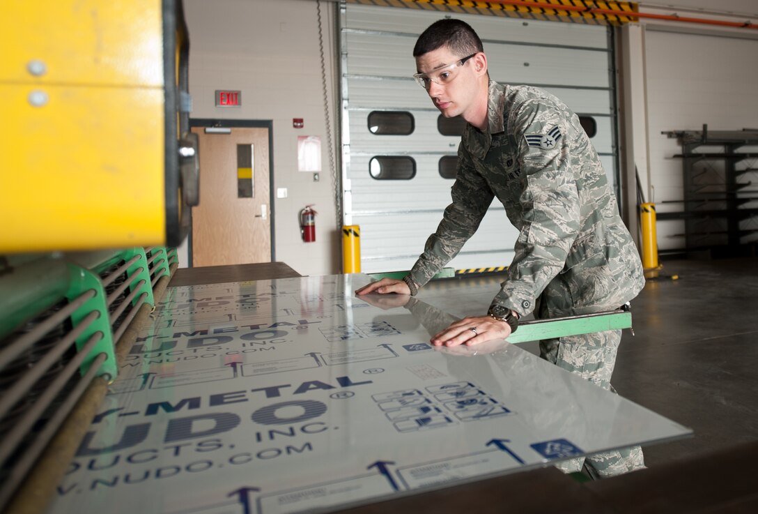 Senior Airman Benjamin Amirault, 28th Civil Engineer Squadron structures technician, inserts a piece of poly-metal into a large hydraulic shear machine for a crosswalk sign at Ellsworth Air Force Base, S.D., Aug. 15, 2013. As a less expensive, more durable alternative to aluminum, poly-metal is used in sign construction. (U.S. Air Force photo by Airman 1st Class Alystria Maurer/Released)