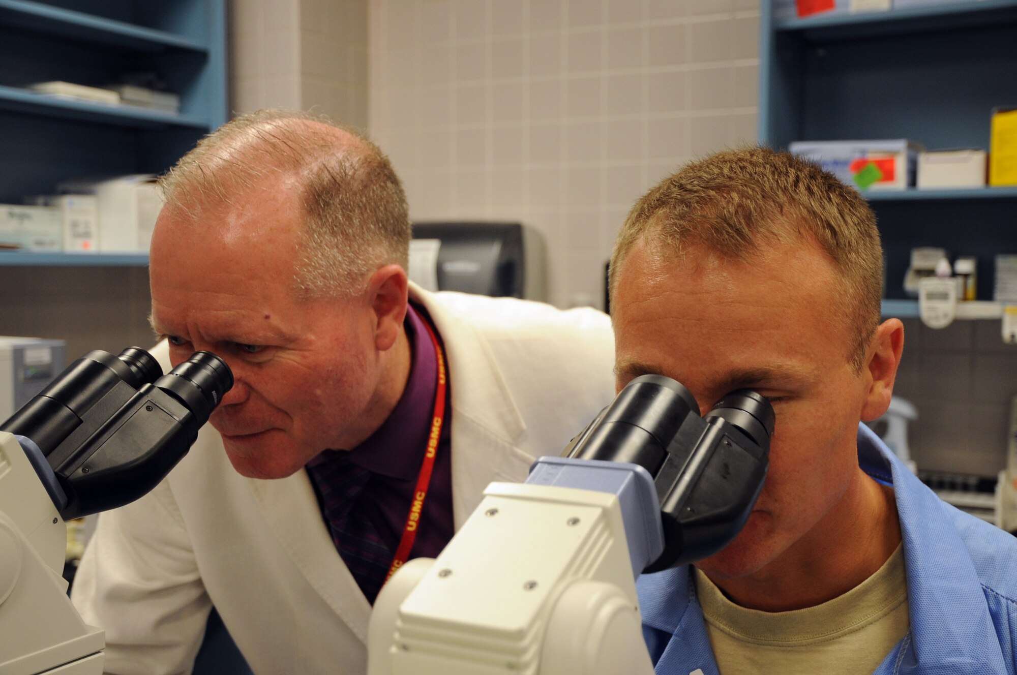 Paul Bennett, American Accreditation for Ambulatory Health Care surveyor, peers through a microscope with Senior Airman Charles Danowski, 319th Medical Support Squadron medical laboratory technican, in the 319th Medical Group clinic on Grand Forks Air Force Base, N.D., Aug. 21, 2013. A three-person AAAHC survey team spent three days checking and inspecting every facet of the clinic's operation. (U.S. Air Force photo/Staff Sgt. David Dobrydney)