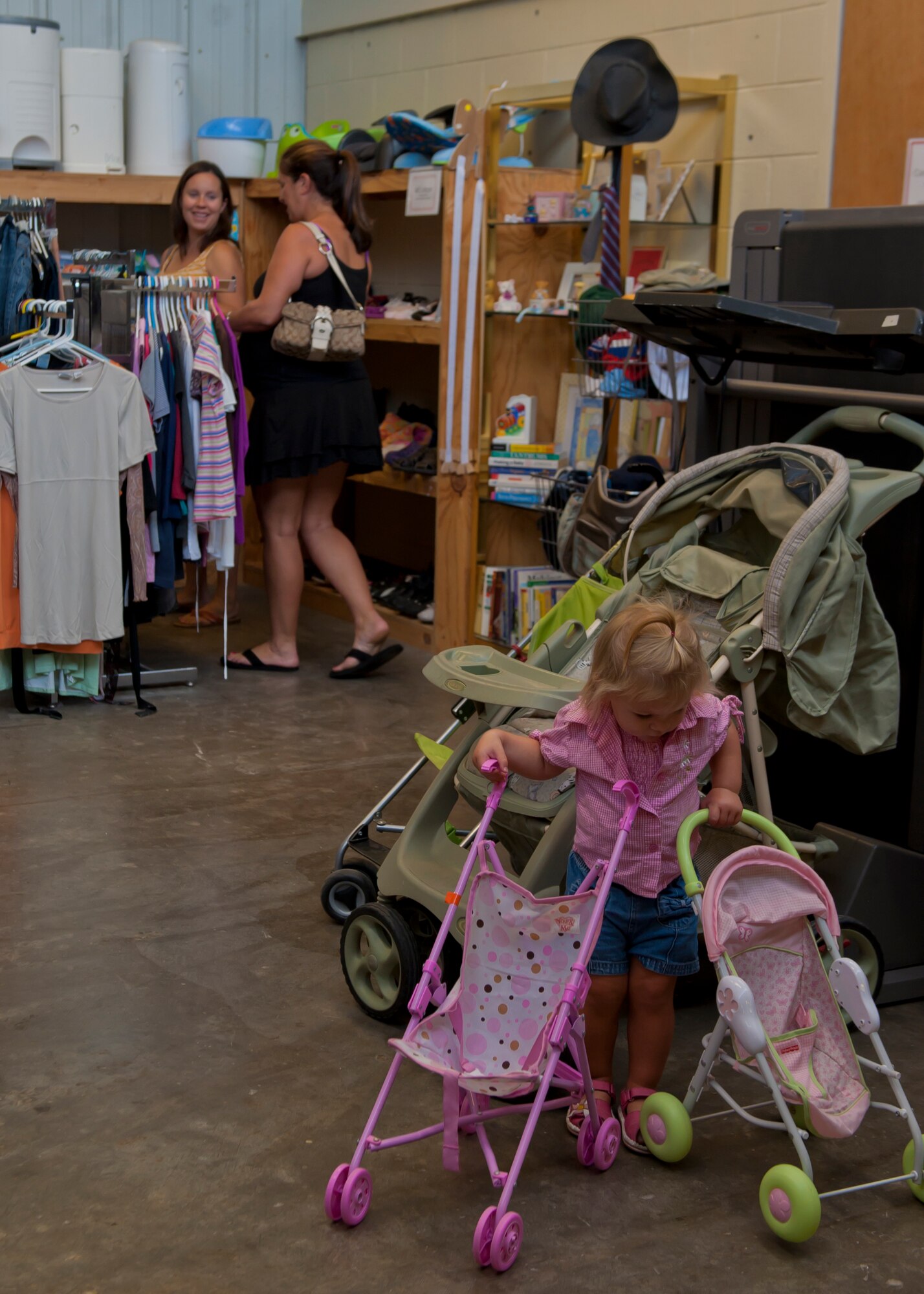A child plays as her mother, Erin, wife of Capt. Richard, 6th Reconnaissance Squadron MQ-1 pilot, shops for a new outfit for her during the Thrift Shop reopening at Holloman Air Force Base, N.M., Aug. 20. The Thrift Shop provides members of Team Holloman a means of acquiring new and gently-used goods at a portion of the cost of the item’s retail value. Last name withheld due to operational safety constraints. (U.S. Air Force photo by Airman 1st Class Aaron Montoya/Released)