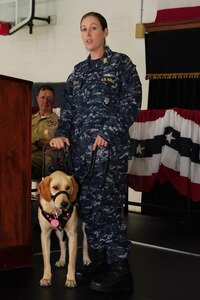 Chief Petty Officer Jeannette Tarqueno, a gunner’s mate and wounded warrior, addresses the audience with her new service dog Gaza, during a ceremony Aug. 26, 2013, at the Naval Consolidated Brig Charleston, S.C. Gaza was trained by NCBC prisoners in conjunction with Carolina Canines for Service, a non-profit organization that trains service dogs for veterans with disabilities. Gaza, a Labrador retriever, will assist Tarqueno by providing more independence and comfort in her life. (U.S. Air Force photo/ Airman 1st Class Chacarra Neal)