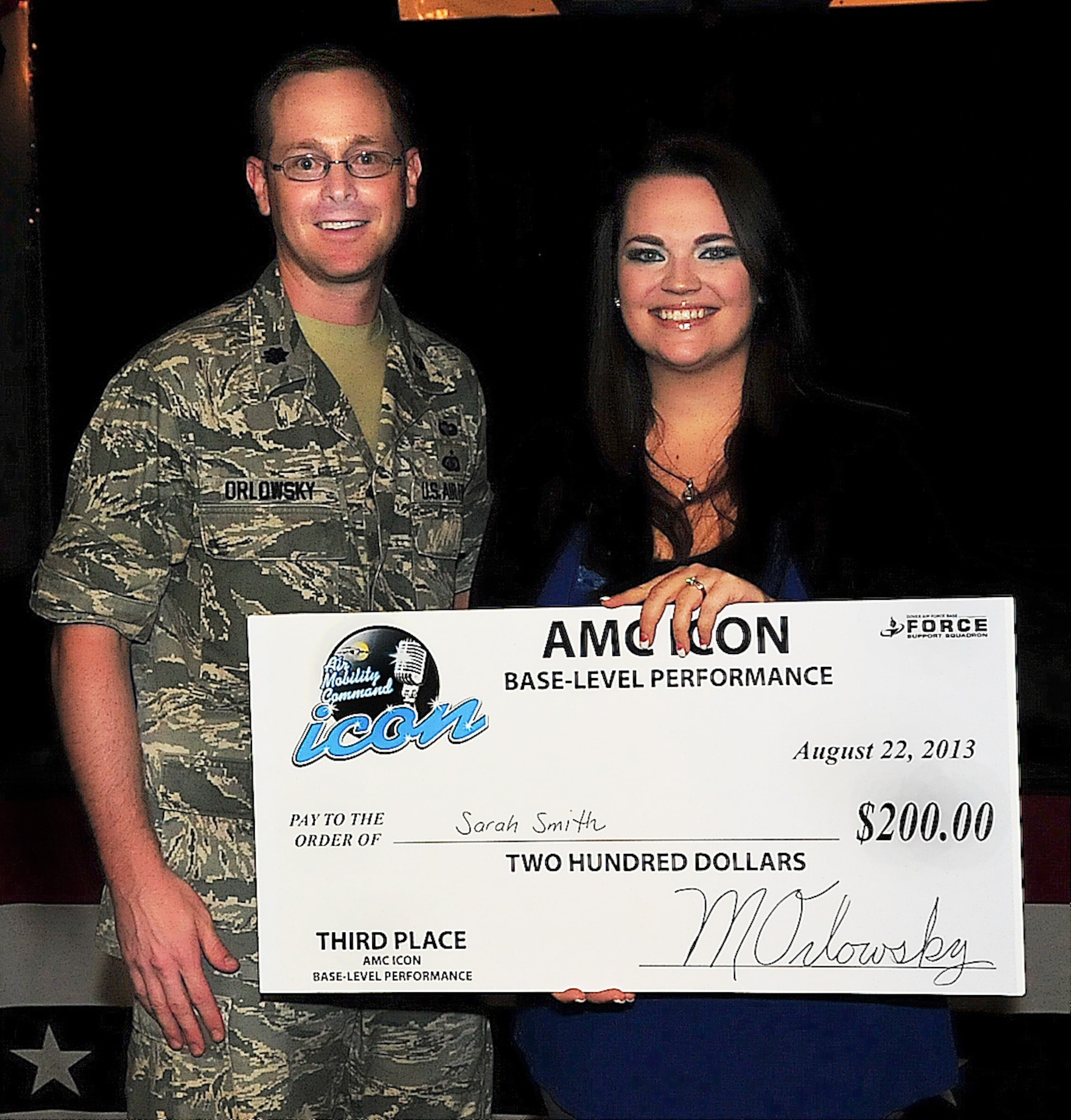 Sarah Smith, spouse of Senior Airman Christopher Smith, receives the 3rd place check from Lt. Col. Matthew Orlowsky, 436th Force Support Squadron commander, at the Air Mobility Command Icon qualifier Aug. 22, 2013, on Dover Air Force Base, Del. AMC Icon is a karaoke type competition similar to American Idol. (U.S. Air Force photo/Airman 1st Class Ashlin Federick)