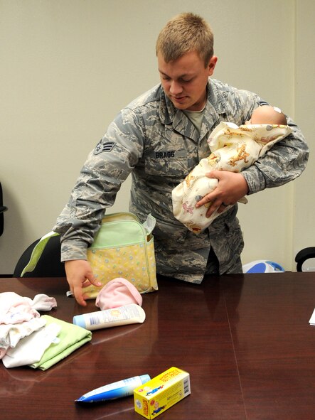 U.S. Air Force Senior Airman Jack Bragg, 7th Communications Squadron, holds a pretend baby while packing a diaper bag during a Dad’s 101 class Aug. 22, 2013, at Dyess Air Force Base, Texas. The purpose of this exercise is to simulate stressors that a dad may face once a newborn baby arrives. (U.S. Air Force photo by Airman Autumn Velez/Released)