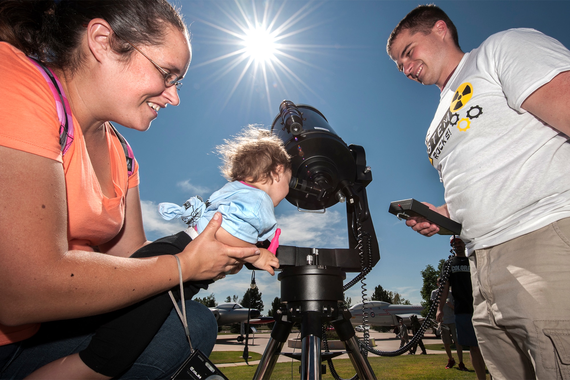 2nd Lt. Michael Hintzman, Air Force Life Cycle Management Center, aims a large telescope at the sun while Melisa Hernandez-Morales holds Elienid Rivera up to view the sun through a special filter at STEM Rocks! The festival was held at the Peterson Air and Space Museum Aug. 24 and included hands-on activities for kindergarten to eighth graders. Some of the activities involved making slime, crawling through caves, launching rockets, building gliders, electricity demonstrations, and more interactive demonstrations. (U.S. Air Force photo/Craig Denton)