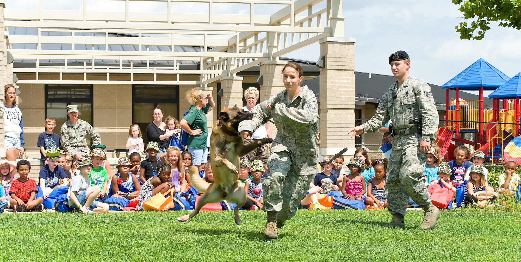 Cuervo, a military working dog, attacks Staff Sgt. Christine Campos, a military working dog trainer with the 436th Security Forces Squadron July 30, 2013, as part of a demonstration during the children's mobility line at Dover Air Force Base, Del. Staff Sgt. John Sutherland, a MWD handler, observes Cuervo to validate his response actions. (U.S. Air Force photo/Roland Balik)
