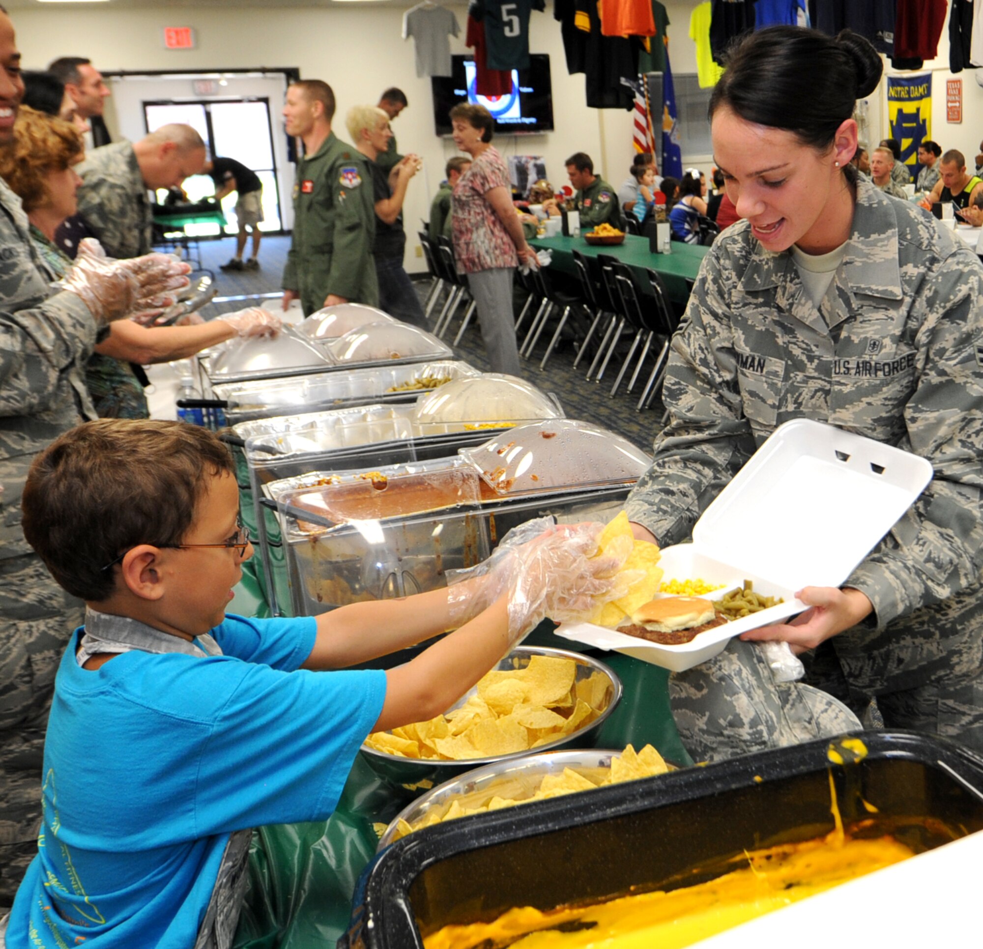 Michael Woodley, left, son of Lt. Col. David Woodley, the 71st Operations Support Squadron commander, serves up chips to Airman 1st Class Marissa Newman, from the 71st Medical Operations Squadron, during the August Singles’ International Gourmet Meal Opportunity at Vance Air Force Base, Okla. (U.S. Air Force photo/ Senior Airman Frank Casciotta)