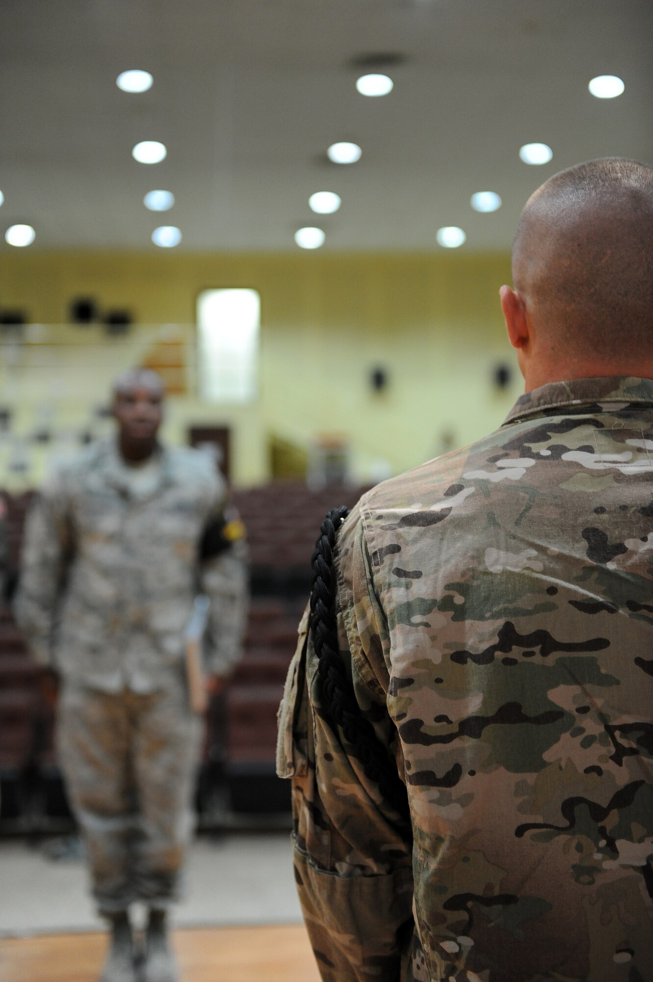 Senior Airman William Leonard, 1st Expeditionary Civil Engineer Group, an aiguillette wearing honor guard member, stands at attention during the opening brief at the start of honor guard practice Aug. 27, 2013 at an undisclosed location in Southwest Asia.  The 386th Air Expeditionary Wing Honor Guard currently has about 30 members, 12 of whom are aiguillette wearers.  Members who wear the aiguillette are experienced honor guard members working toward the honor guard brassard seen on honor guard noncommissioned officer Tech. Sgt. Kareem Edwards pictured in the background.  Aiguillette wearers are used as trainers for the newer members of the team.  (U.S. Air Force photo by Master Sgt. Marelise Wood)