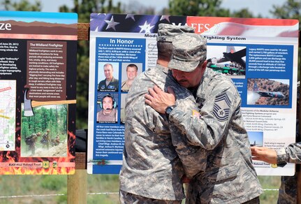 Maj. Gen. Gregory Lusk, adjutant general of the North Carolina National Guard, left, hugs Chief Master Sgt. Andy Huneycutt, MAFFS-7 crew member, during the unveiling of an interpretive sign near Edgemont, S.D., July 1, 2013, that honors the airmen of the North Carolina Air National Guard C-130 aircraft that crashed while supporting the White Draw Fire one year ago this day.