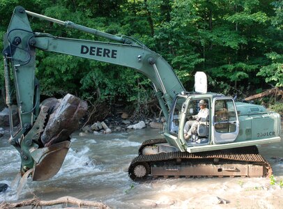 Pfc. Joshua Haller, a member of the New York Army National Guard's 827th Engineer Company, uses a hydraulic excavator July 3, 2013, to remove a boulder and other flood debris from Fulmer.