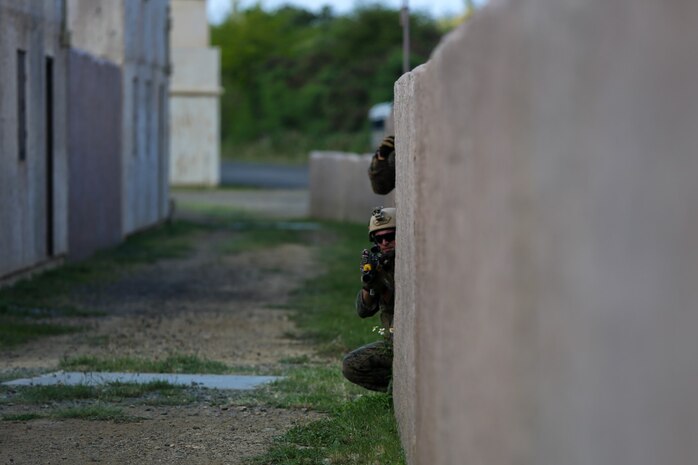 Marines serving with Alpha Company, 1st Reconnaissance Battalion, take cover behind a wall during a mission rehearsal exercise here, Aug. 20, 2013. Marines responded to simulated small-arms fire and artillery rounds with suppressing fire and patrols through the area. An evaluator followed each squad of Marines and assessed their various skills including tactics, coordination and execution during the mission.