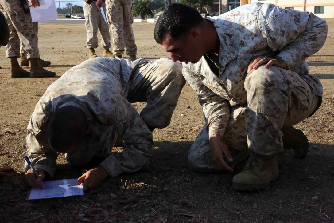 Cpl. Alec A. Richardson, field instructor, Field Company, Weapons Field Training Battalion, helps out another instructor describe and draw several objects the squads were shown at the beginning of the competition at Edson Range aboard Marine Corps Base Camp Pendleton, Calif., Aug. 23. The memory game is called K.I.M or Keep In Memory.