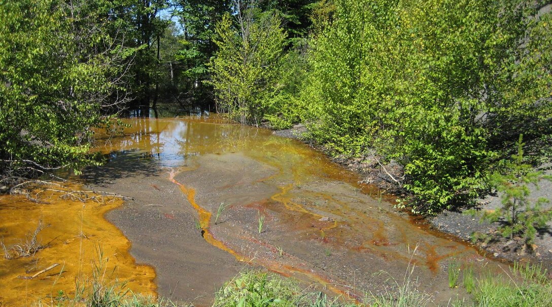 A degraded Pennsylvania stream that has been impacted by acid mine run off from an abandoned coal mine. The reddish/orange color is a result of acid mine drainage.
