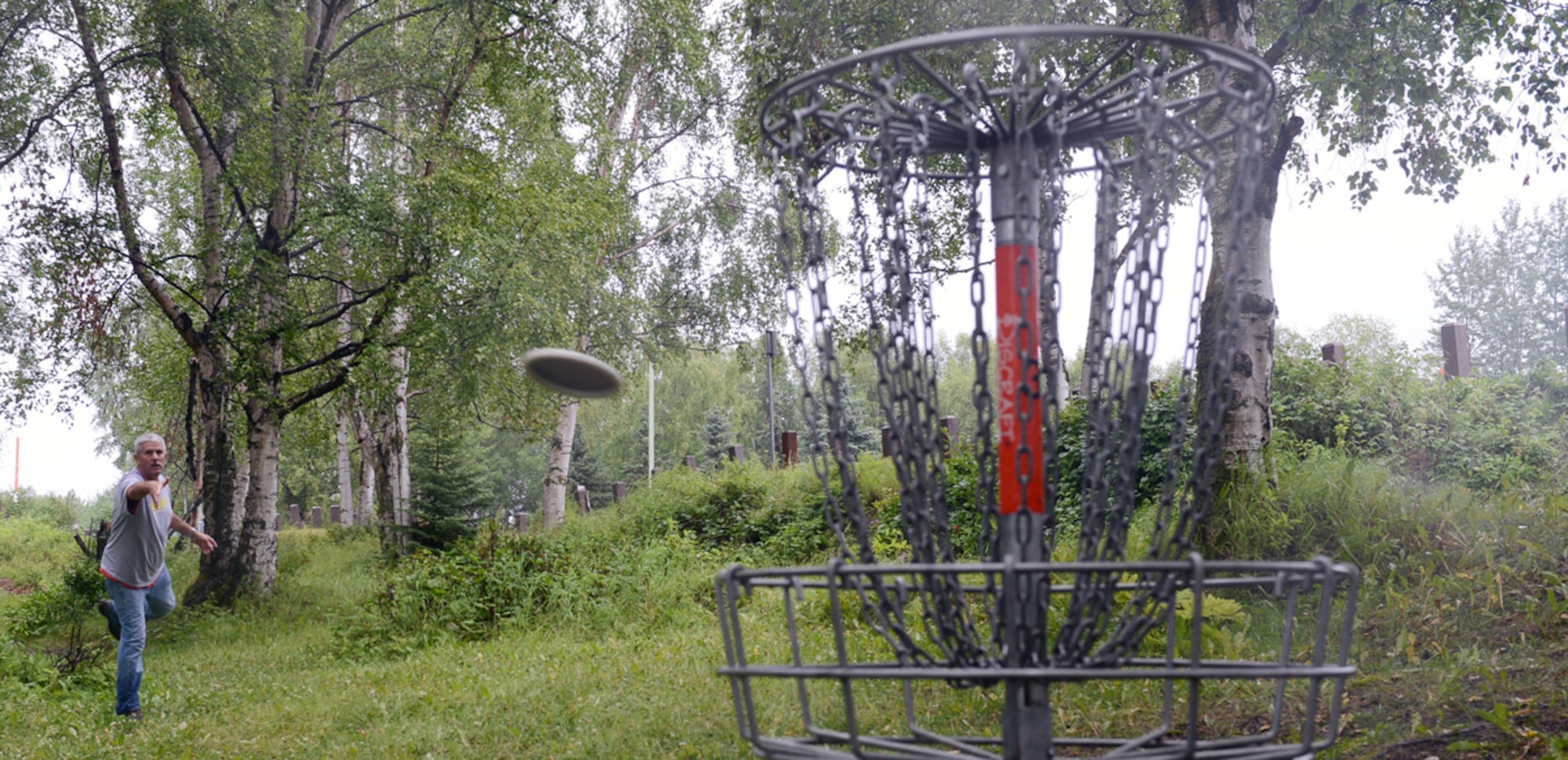 JOINT BASE ELMENDORF-RICHARDSON, Alaska -- National Guardsman Tech. Sgt. Larry Kirk tosses a disc into a standard disc golf basket at the Russian Jack Springs golf course August 12. Kirk is beginning his 50-states tour across the U.S. to promote the game. He is also attempting the Guinness World Record for most courses completed in a year. Kirk is a native of Whittier,Calif. (U.S. Air Force photo/Airman Ty-Rico Lea)