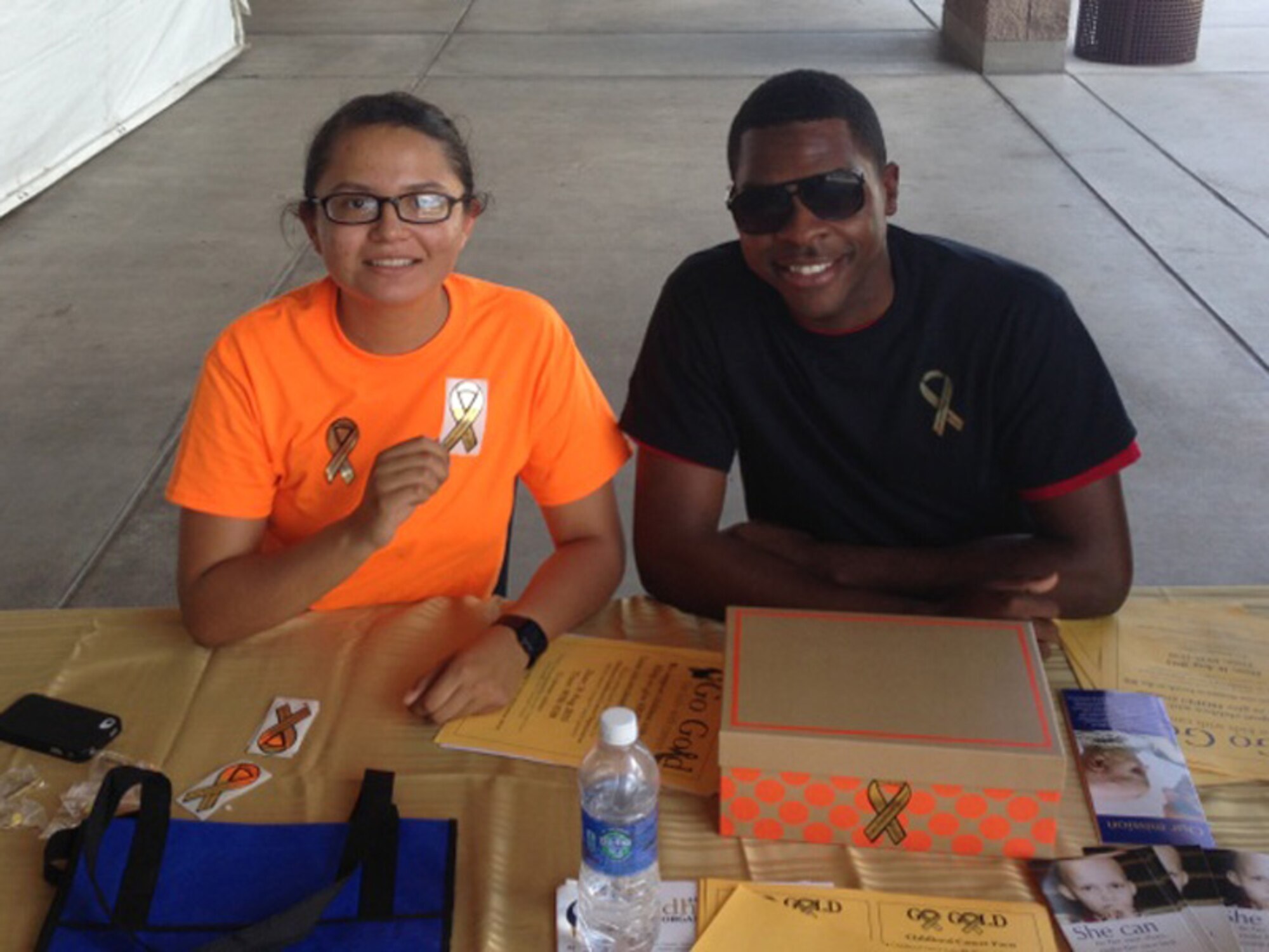 Airman 1st Class Rocio Pattarroyo, 355th Communications Squadron knowledge operations manager, and Airman 1st Class Lorenzo Kates, 41st Electronic Combat Squadron knowledge operations manager, sit behind a donation booth at the Base Exchange on Davis-Monthan Air Force Base, Ariz., August 16, 2013. In six hours, the Airmen raised over $1000 for the American Childhood Cancer Organization. (Courtesy photo)