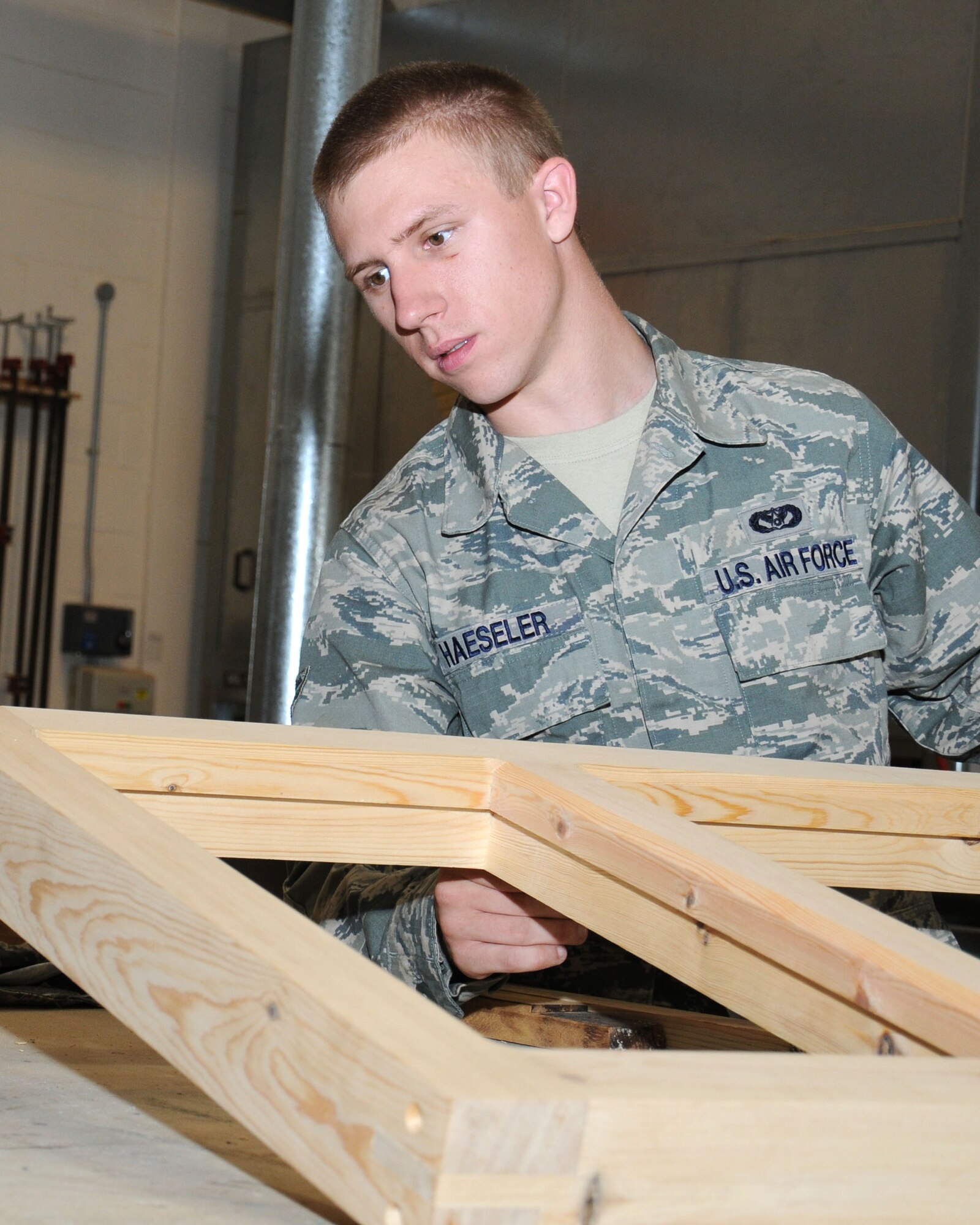 Airman 1st Class Scott Haeseler, 100th Civil Engineer Squadron structures journeyman from Mystic, Conn., tests his skills by making a timber window frame Aug. 27, 2013, on RAF Mildenhall, England. In the structures shop, David Spragg, 100th CES structures charge hand carpenter and joiner from Yorkshire, England, gives workshop machine training to military and civilian personnel. In making a new timber window frame, the member being trained uses eight machines. (U.S. Air Force photo by Gina Randall/Released)