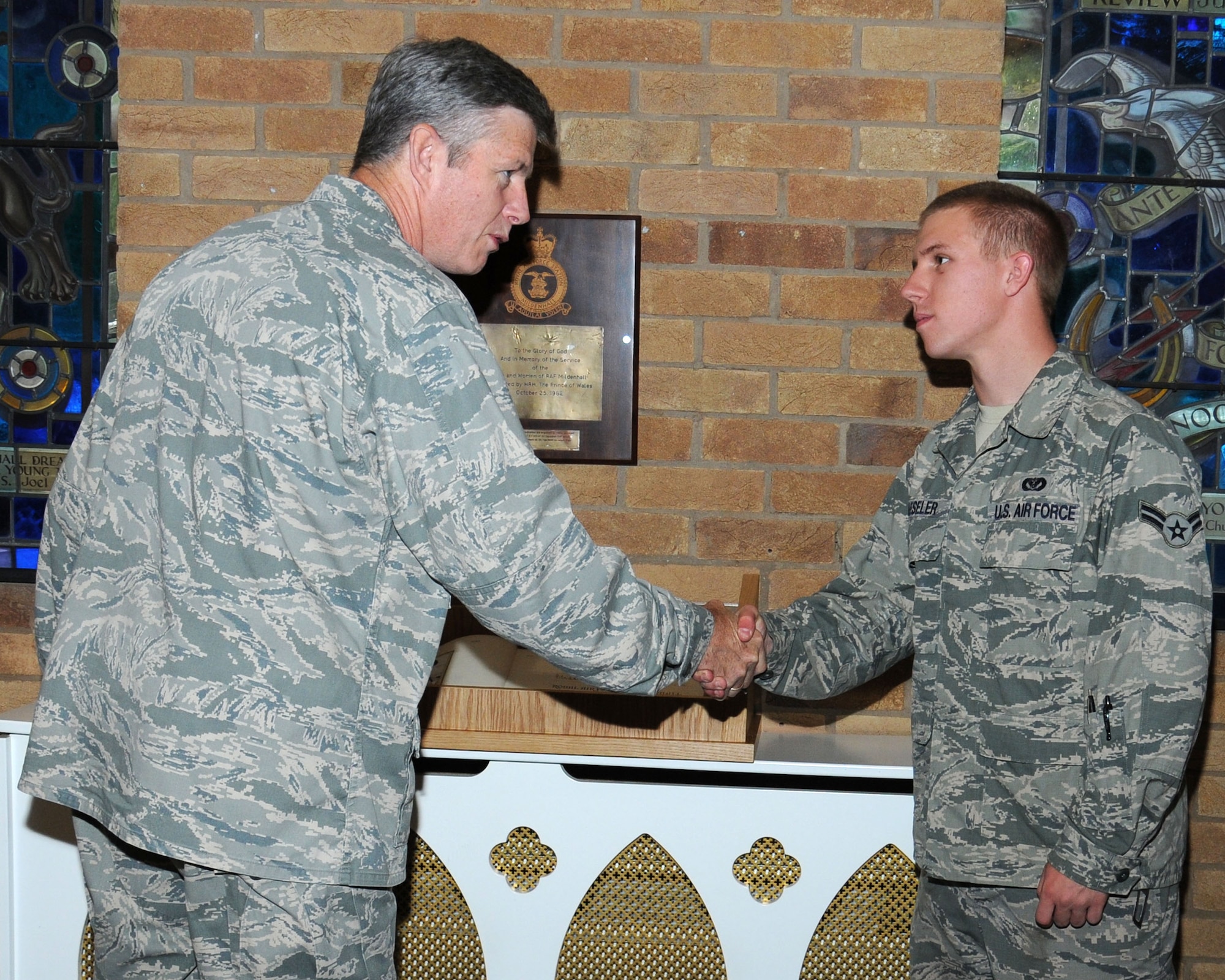 U.S. Air Force Lt. Col. Henry Close, left, 100th Air Refueling Wing chaplain, coins Airman 1st Class Scott Haeseler, 100th Civil Engineer Squadron structures journeyman from Mystic, Conn., Aug. 27, 2013, in the chapel on RAF Mildenhall, England. In 1982, His Royal Highness, the Prince of Wales, signed the official RAF Station Book on RAF Mildenhall. The cabinet housing the book had a broken piece of glass in it, and Haeseler helped David Spragg, 100th CES structures charge hand carpenter and joiner from Yorkshire, England, manufacture a new case out of materials left over from other base projects. (U.S. Air Force photo by Gina Randall/Released)