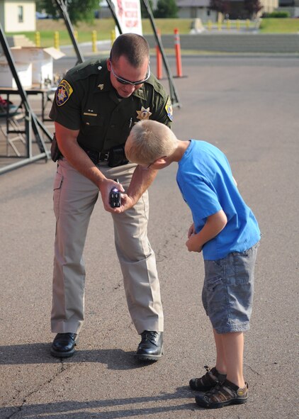 Joe Kinsey, a Montana State Trooper, shows Trevor Seals, 9, how his Taser works during the Rolling Thunder motorcycle safety event Aug. 27 at the old Base Exchange parking lot.  Kinsey attended the event to give motorcycle riders a safety brief before they headed out on a 130-mile-long mentorship ride.  (U.S. Air Force photo/Senior Airman Cortney Paxton)