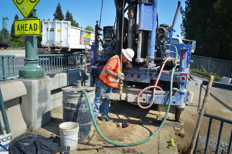 A contractor for the U.S. Army Corps of Engineers Sacramento District inspects a newly-drilled hole on the Watt Avenue bridge in Sacramento Calif., July 25, 2013. Holes across the bridge provide access to the levee beneath, where crews will install a seepage cutoff wall.