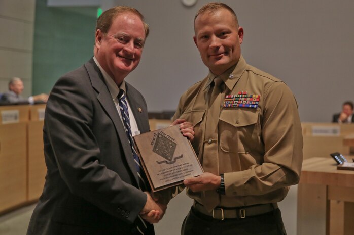 Lt. Col. Lance Jackola, the commanding officer of 1st Battalion, 1st Marine Regiment, presents Mayor Keith Curry with a plaque, thanking him and the community for the continued support of the battalion during a meeting here, Nov. 26, 2013. The community is celebrating its 10-year anniversary of adopting the battalion. In addition to homecoming events, mess nights, fund raisers and care packages, the community supports families visiting wounded Marines by helping with travel costs, hotel accommodations and meals.