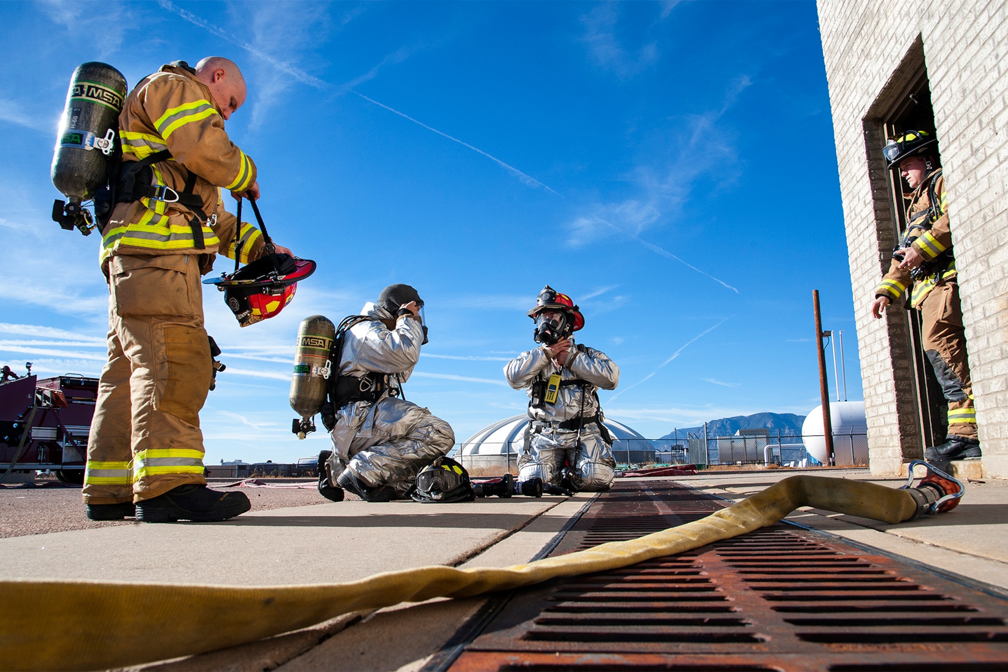 PETERSON AIR FORCE BASE, Colo. -- Firefighters from the 21st Civil Engineer Squadron fire department prepare to enter a structural training facility. Fire fighters used this training to practice different firefighting techniques and spray patterns, and are able to see first-hand how effective it is on a fire. Firefighters require at least 300 gallons of water per minute from a line when fighting a fire. The silver proximity gear reflects heat and is used primarily for aircraft fires but can be used in other fire situations. The gold suit is used to fight structural fires. (U.S. Air Force photo/Craig Denton)