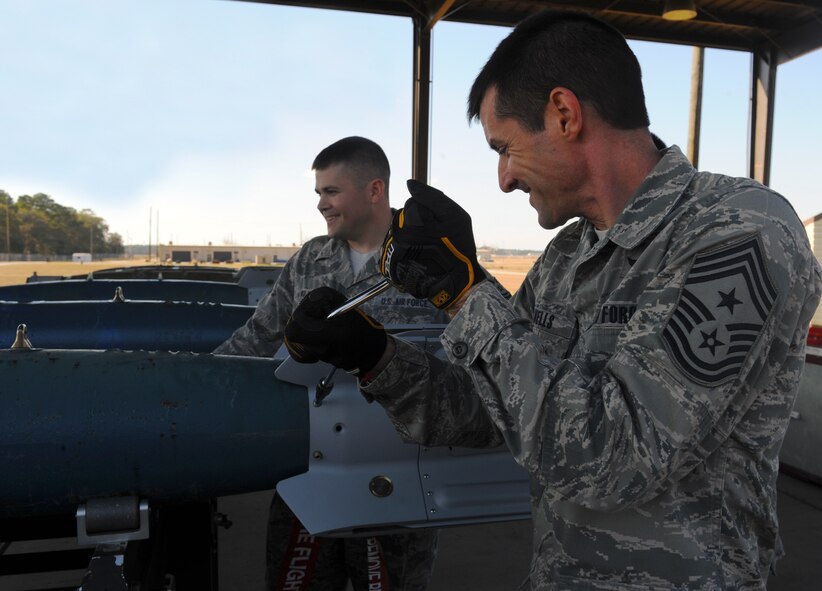 U.S. Air Force Chief Master Sgt. Matthew Wells, 23d Wing command chief, jokes with Tech. Sgt. Derek Williams, 23d Equipment Maintenance Squadron munitions systems technician, while tightening the fin assembly on the practice GBU-12 laser-guided bomb at Moody Air Force Base, Ga., Dec. 2, 2013. While visiting the 23d EMS munitions flight, Wells and Col. Chad Franks, 23d WG commander, received a bomb-build demonstration and built two bombs. (U.S. Air Force photo by Senior Airman Olivia Bumpers/Released)