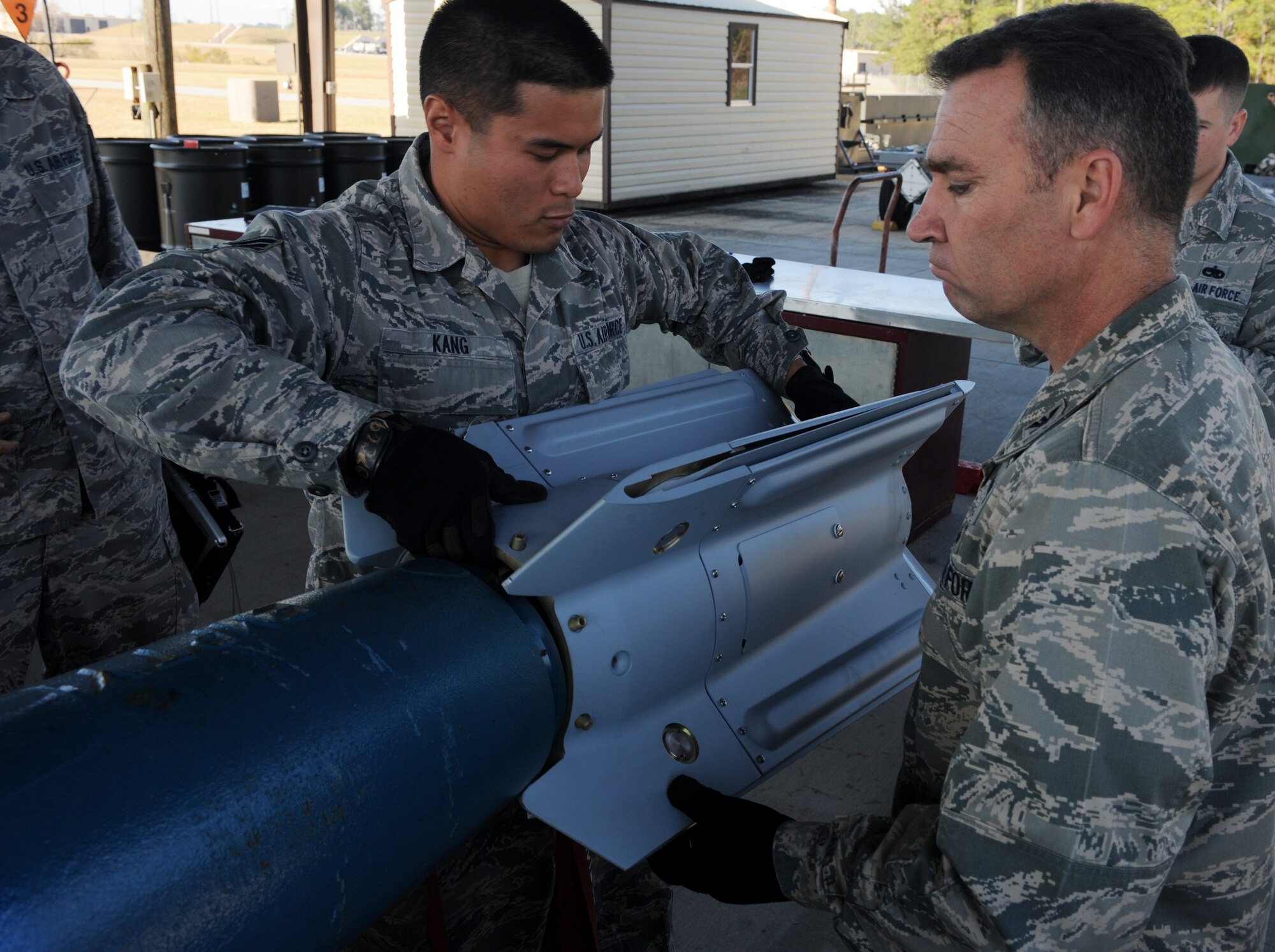 U.S. Air Force Senior Airman Vattanak Kang, 23d Equipment Maintenance Squadron munitions systems technician, assists Col. Chad Franks, 23d Wing commander, in placing the fin assembly on the practice GBU-12 laser-guided bomb at Moody Air Force Base, Ga., Dec. 2, 2013. After unpacking the parts, the23d EMS munitions flight places them near the corresponding bomb for faster production. (U.S. Air Force photo by Senior Airman Olivia Bumpers/Released)