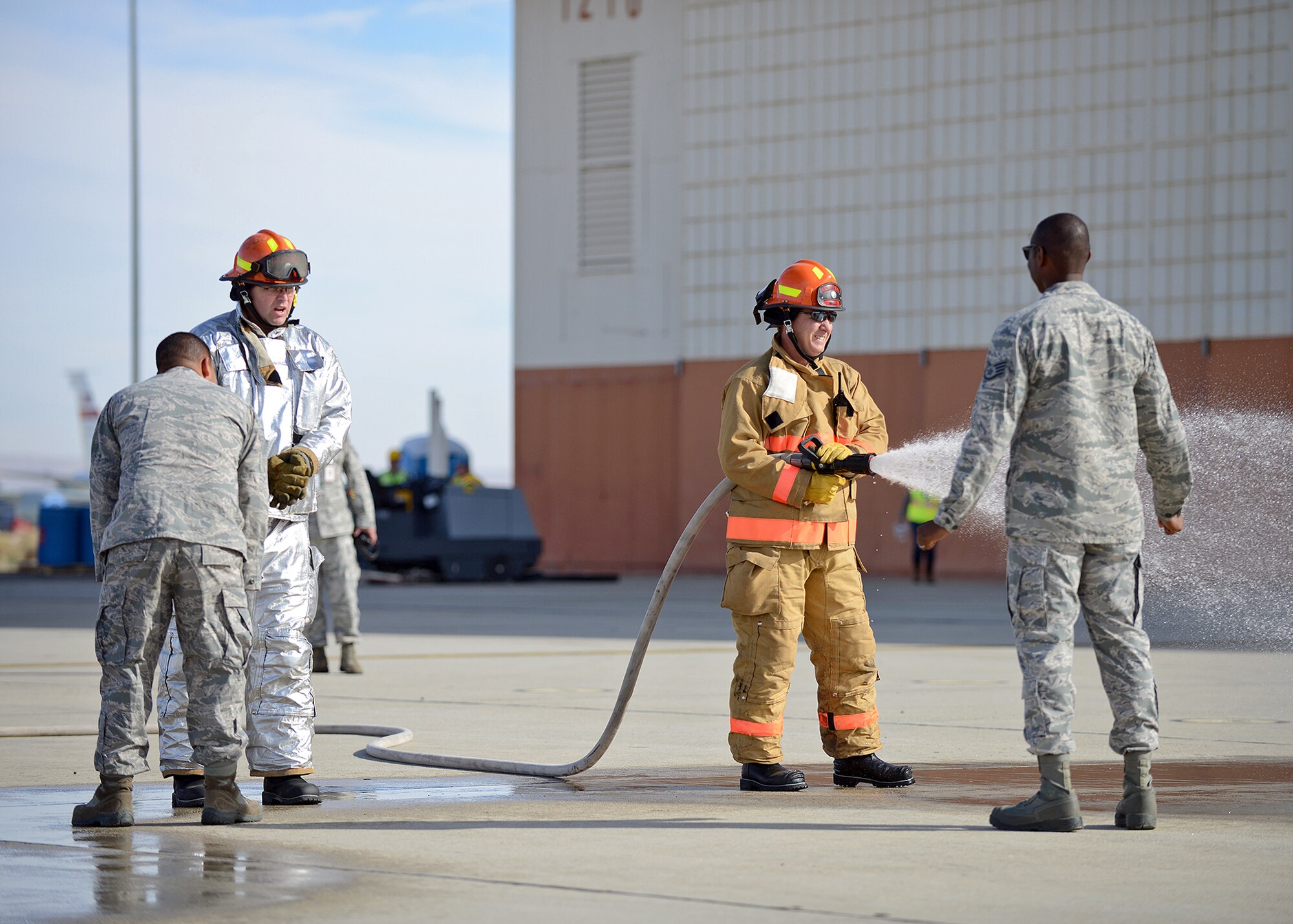 Jeffrey Miles, 412th Civil Engineering Directorate firefighter, simulates spraying down exercise participants as part of the decontamination process during an emergency scenario exercise Nov. 26 in front of Hangar 1210. The purpose of the exercise was so Exercise Evaluation Team members could assess how on-base emergency response personnel gain and maintain control of a site after a fire suppression system discharge incident has occurred. (U.S. Air Force photo by Jet Fabara)