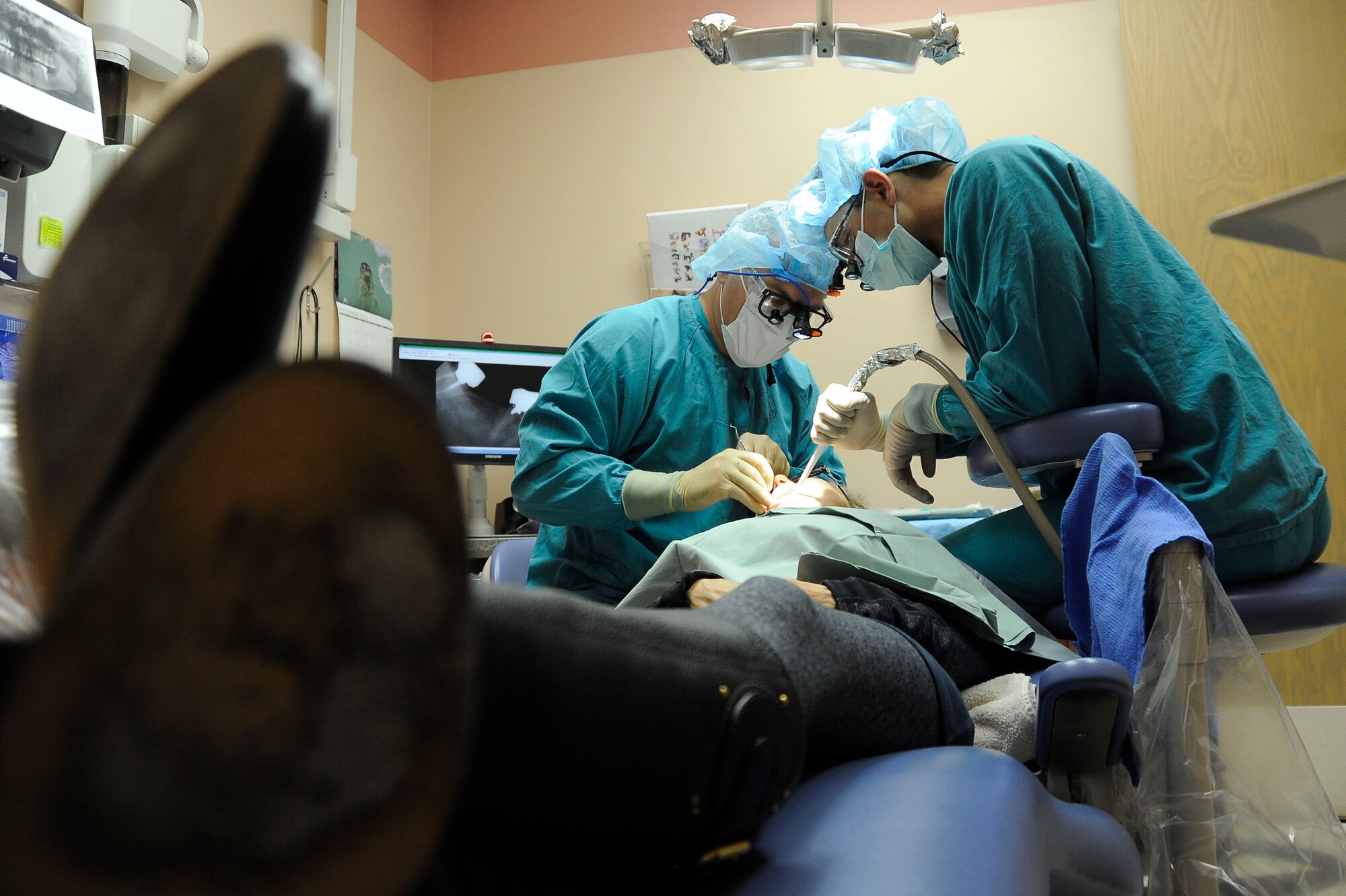 Lt. Col. (Dr.) Jody Harrison, 99th Dental Squadron chief of periodontics (left) and Capt. (Dr.) Andrew Benfield , 99th Dental Squadron  Advanced Education in General Dentistry resident (right), 99th Dental Squadron dentists, perform a dental procedure on a patient Dec. 2, 2013, at Nellis Air Force Base, Nev. Cavities are one of the most common causes for someone to require dental work. (U.S. Air Force photo by Airman 1st Class Timothy Young)