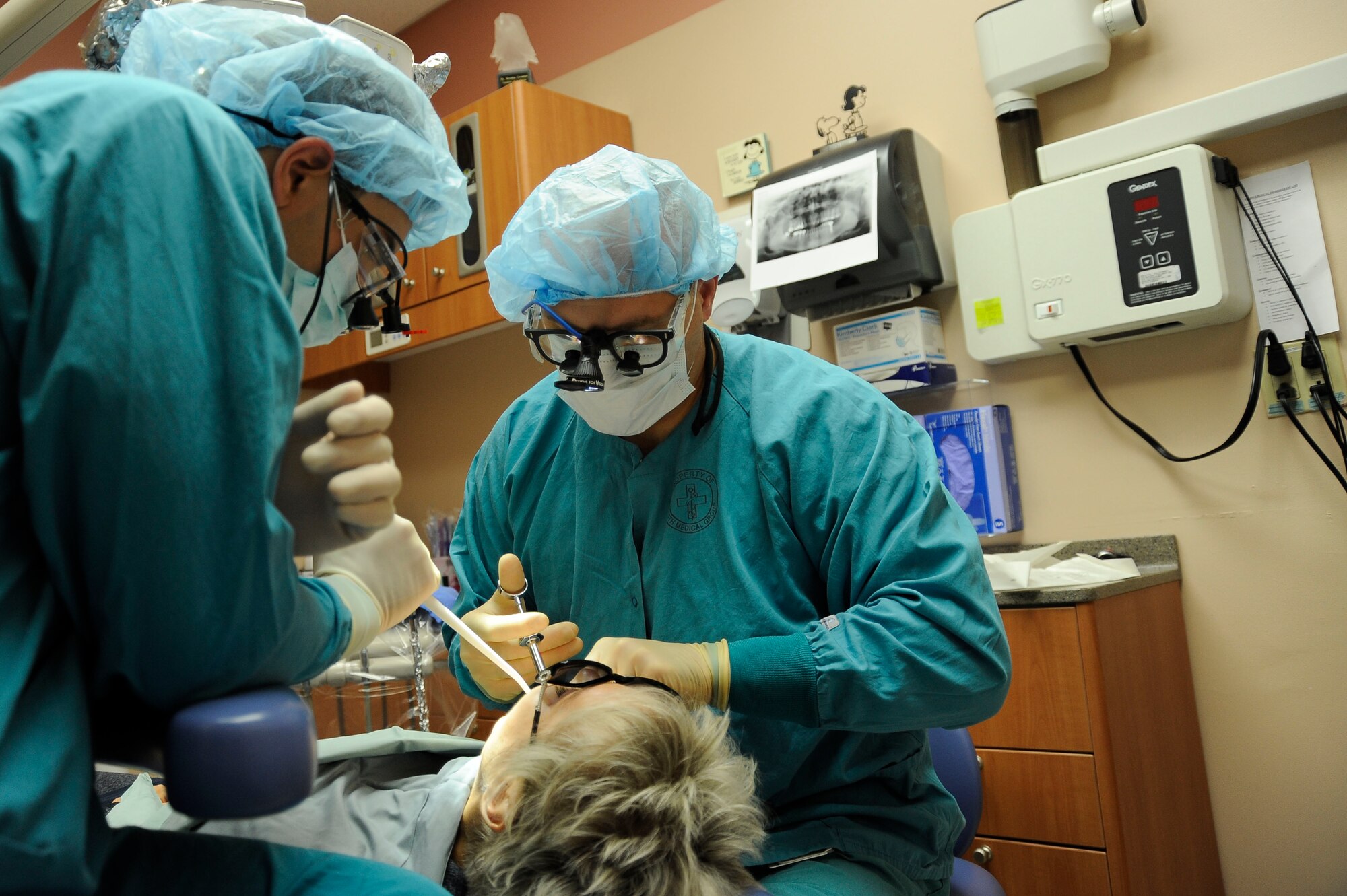 Capt. (Dr.) Andrew Benfield , 99th Dental Squadron  Advanced Education in General Dentistry resident (left) and Lt. Col. (Dr.) Jody Harrison, 99th Dental Squadron chief of periodontics (right), perform a dental procedure on a patient Dec. 2, 2013, at Nellis Air Force Base, Nev. Cavities are one of the most common causes for someone to require dental work. (U.S. Air Force photo by Airman 1st Class Timothy Young)