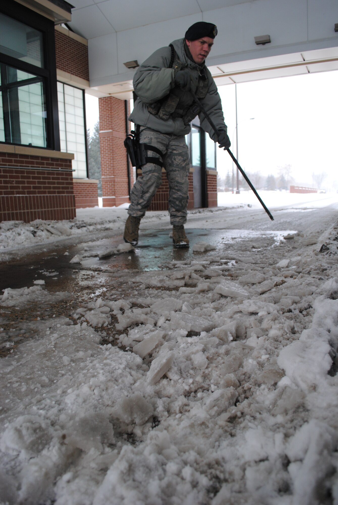 Senior Airman Richard Stafford, 319th Security Forces installation entry controller, breaks chunks of ice from the road section at the main gate of Grand Forks Air Force Base, N.D., Dec. 4, 2013. Periodic breaking and removal of the snow and ice helps inbound vehicles gain better traction, decreases the chances of tail whipping and helps traffic flow smoother through the gate. (U.S. Air Force photo/Staff Sgt. Luis Loza Gutierrez) 
