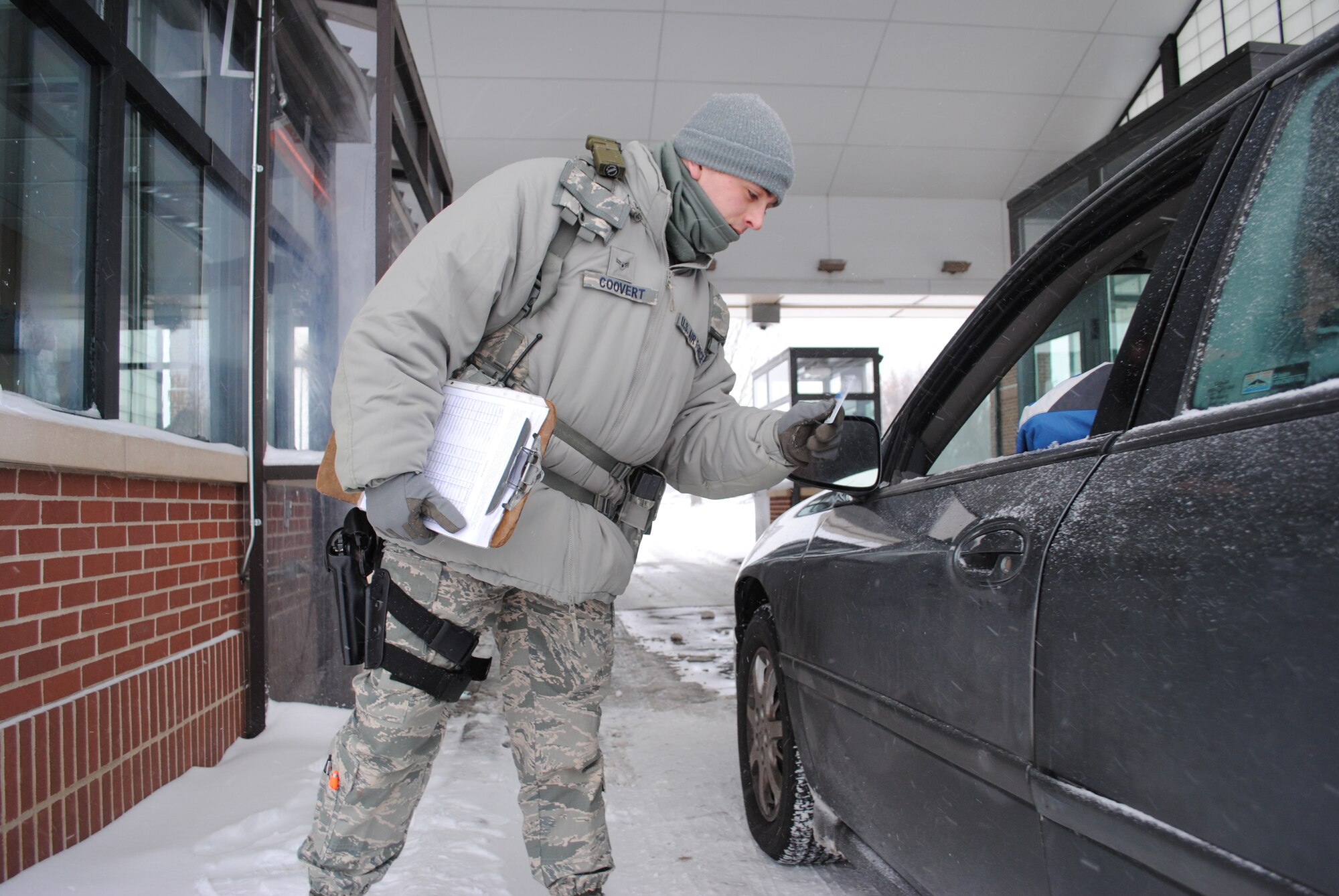 Airman 1st Class Tyler Coovert, 319th Security Forces installation entry controller, checks a motorist for proper identification at main gate of Grand Forks Air Force Base, N.D., Dec. 4, 2013. Coovert and other entry controllers had to check long lines of vehicles later than usual Wednesday morning because delayed reporting was initiated as safety measure due to the severe winter weather. (U.S. Air Force photo/Staff Sgt. Luis Loza Gutierrez) 
