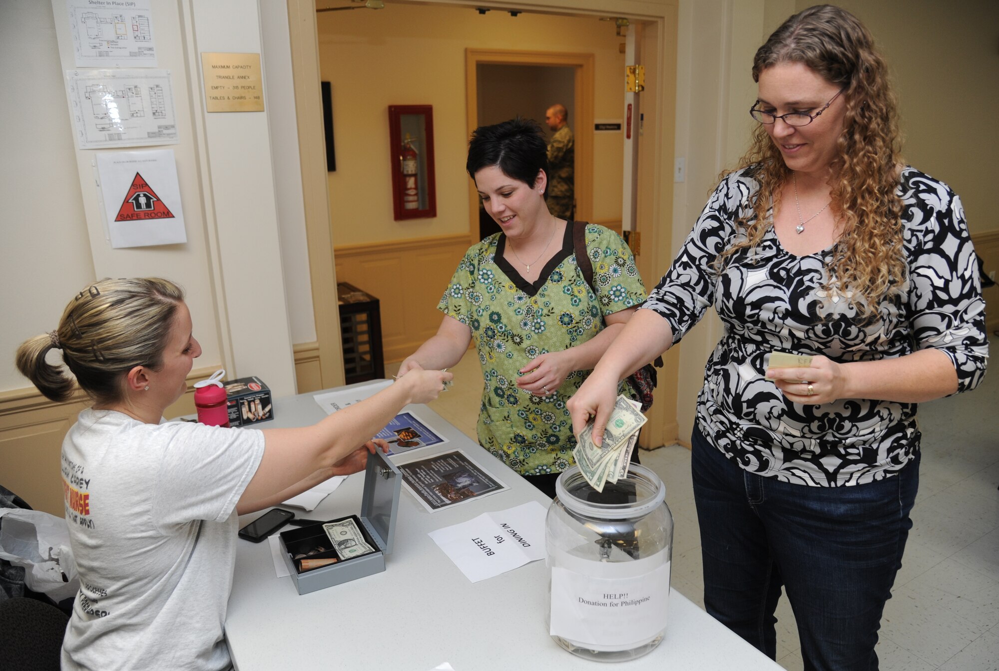 First Lt. Aftan Boudreaux, 81st Force Support Squadron, gives change to Kimberly Echtle, 81st Medical Operations Squadron, for purchasing 15 plates of food as Kim Griffitt, 81st MDOS, deposits a donation of $150.00 from her squadron during an Asian-Pacific American Heritage Committee’s fundraiser for the Red Cross international typhoon recovery efforts Dec. 4, 2013, at the Triangle Chapel Annex, Keesler Air Force Base, Miss.  Committee members cooked a menu of chicken Adobo, pancit, lumpia and steamed/fried rice. Volunteers from the American Red Cross sold the plates of food to raise money for typhoon recovery efforts. (U.S. Air Force photo by Kemberly Groue)