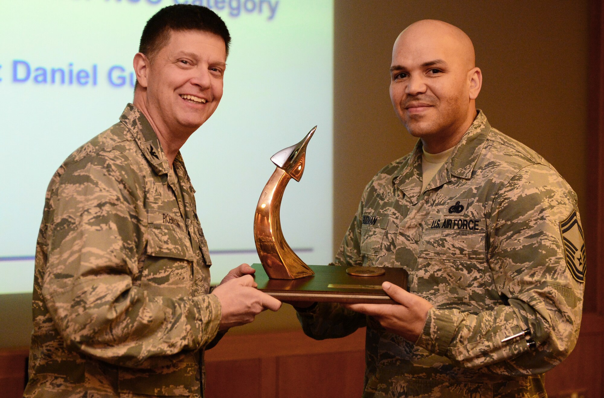 Col. Kyle Robinson, 48th Fighter Wing commander, presents Senior Master Sgt. Daniel Guzman, 48th Logistics Squadron material management flight chief, with the Gen. Lew Allen Jr. Trophy during the bi-monthly wing staff meeting at Royal Air Force Lakenheath, England, Dec. 2, 2013. The trophy was awarded for the first time in 2013 to a base-level officer and Senior NCO in Logistics Readiness career field. (U.S. Air Force photo by Airman 1st Class Dawn M. Weber/Released)