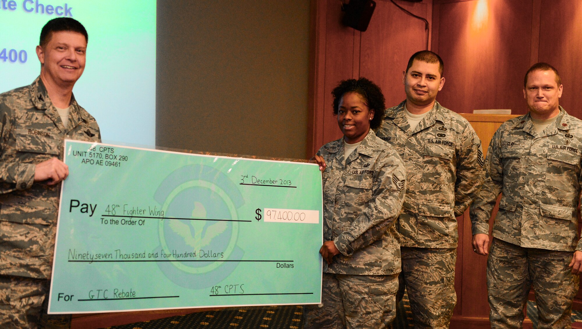 Airmen from the 48th Comptroller Squadron present Col. Kyle Robinson, 48th Fighter Wing commander, with a rebate check of $97,400 during the bi-monthly wing staff meeting at Royal Air Force Lakenheath, England, Dec. 2, 2013. The rebate was awarded to RAF Lakenheath for the efficient success of the base Government Travel Card program. (U.S. Air Force photo by Airman 1st Class Dawn M. Weber/Released)