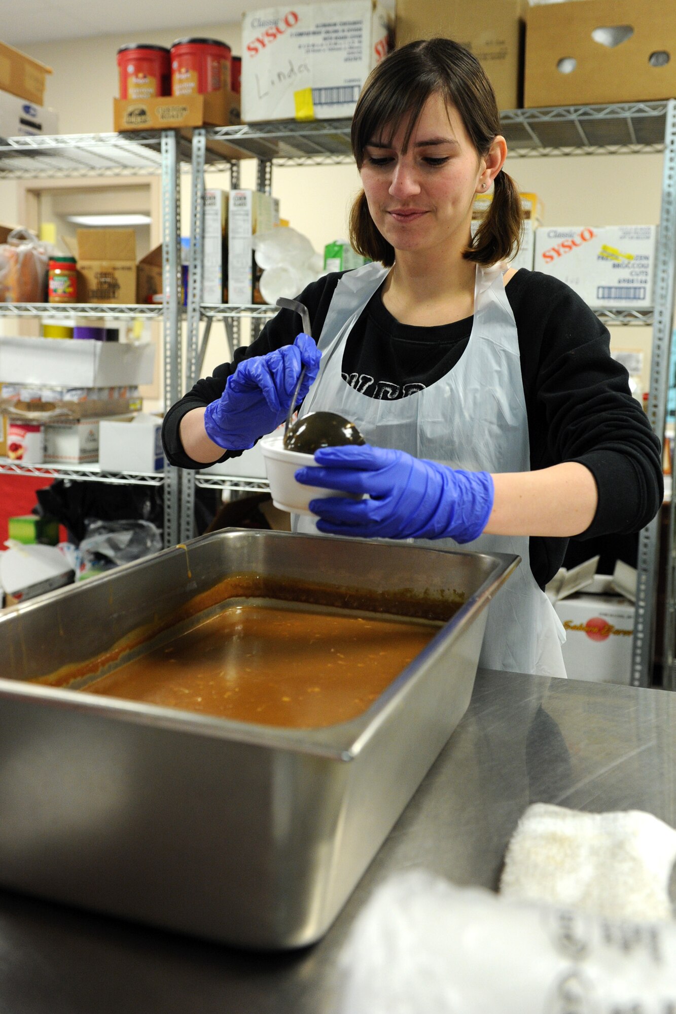 Senior Airman Kristina Chrobak, 341st Force Support Squadron relocations technician, pours gravy into a container before preparing it for delivery at the Great Falls Community Food Bank on Nov. 28. Chrobak was the event coordinator from Malmstrom Air Force Base, responsible for finding Airmen to volunteer their time by cooking, preparing and delivering Thanksgiving meals. (U.S. Air Force photo/Senior Airman Katrina Heikkinen)