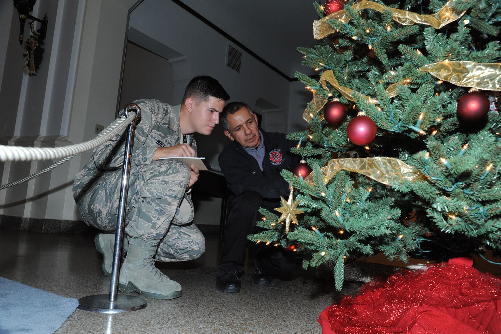 Staff Sgt. Allen Roby and Jesus Lopez, 902nd Civil Engineer Fire Department inspectors, perform a safety inspection on the holiday tree in the Joint Base San Antonio-Randolph Taj Mahal.(U.S. Air Force photo by Rich McFadden)