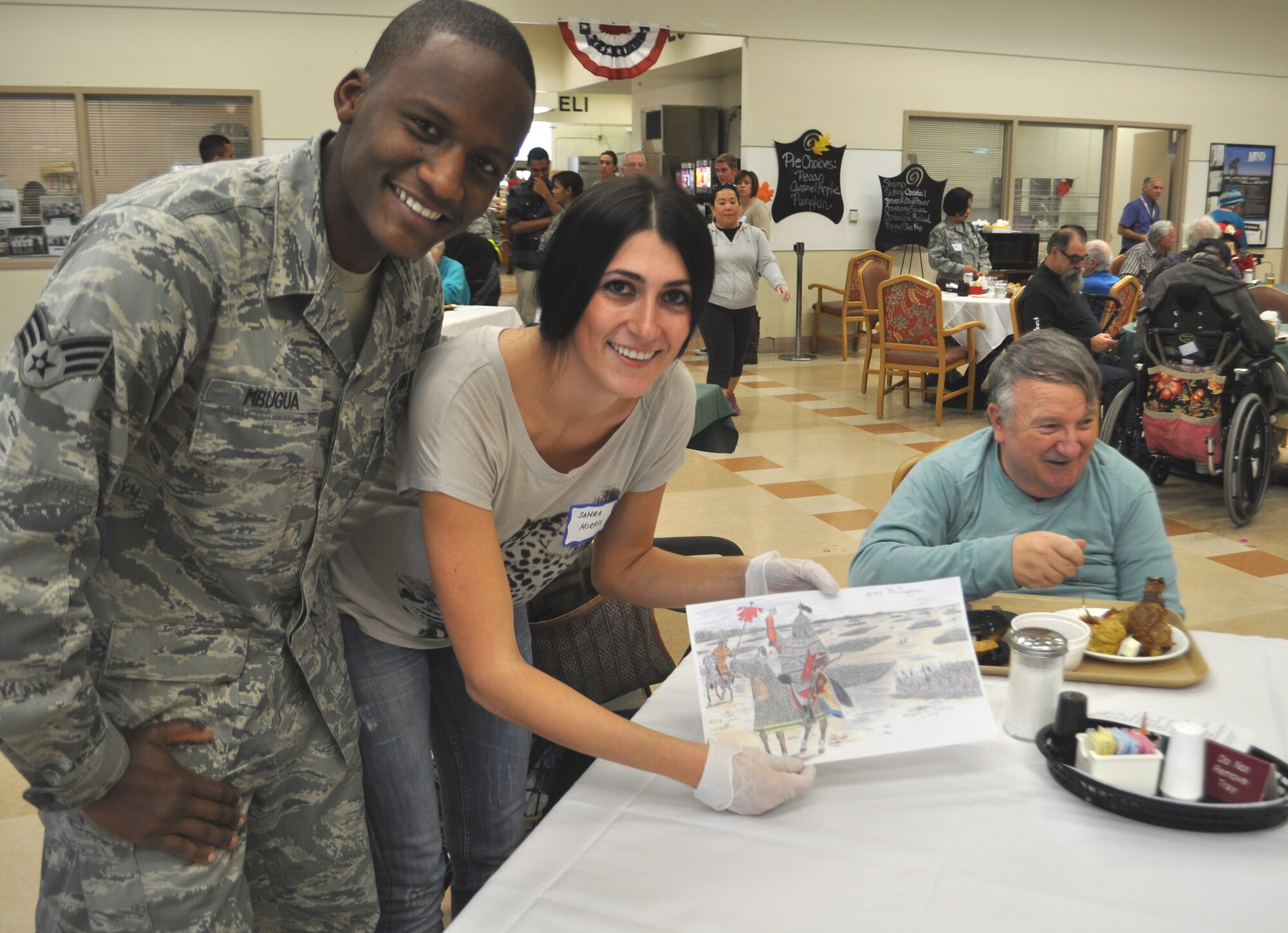 Senior Airman Joseph Mbugua, 60th Logistics Readiness Squadron, and
volunteer Samra Norris, show off the artwork of Ron sitting behind them. Ron
is just one of 900 veterans and their families who were served their
Thanksgiving dinner by a group of volunteers from the 60th and 349th Air
Mobility Wings at Travis Air Force Base. For a number of years, the Reserve
wing has coordinated the volunteer effort to spend Thanksgiving with the
Yountville Veterans Home, so they can serve and spend time with them on this
holiday.  (U.S. Air Foce photo/Ellen Hatfield)