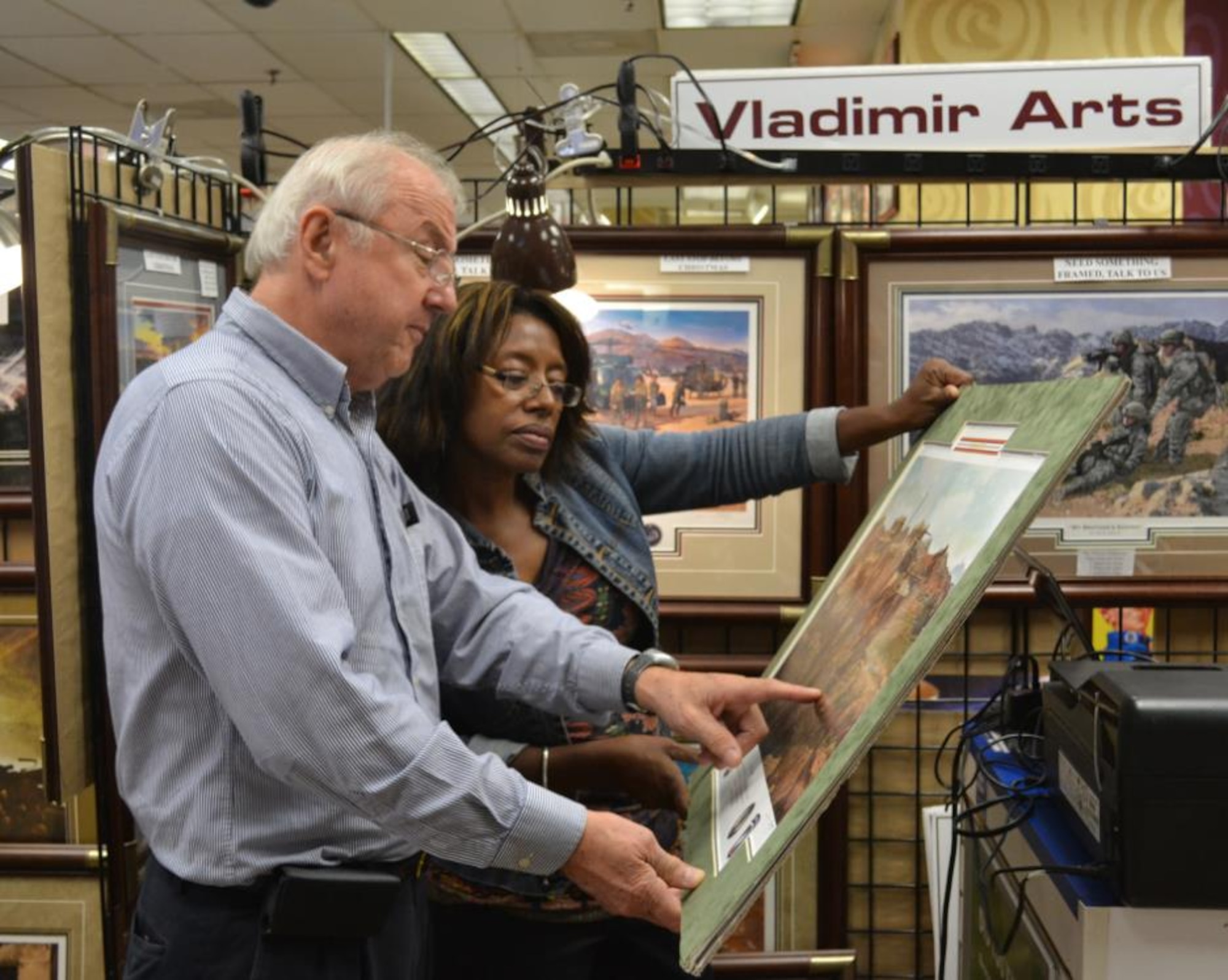 Lew Iwlew, owner of Vladimir Arts, explains the history of a painting to a customer Sept. 14, 2013, at the post Exchange, Fort George G. Meade, Md. Vladimir Arts specializes in military-themed art work and can be found at various AAFES locations. (U.S. Air Force photo by 2nd Lt. Carrie Volpe/Released)
