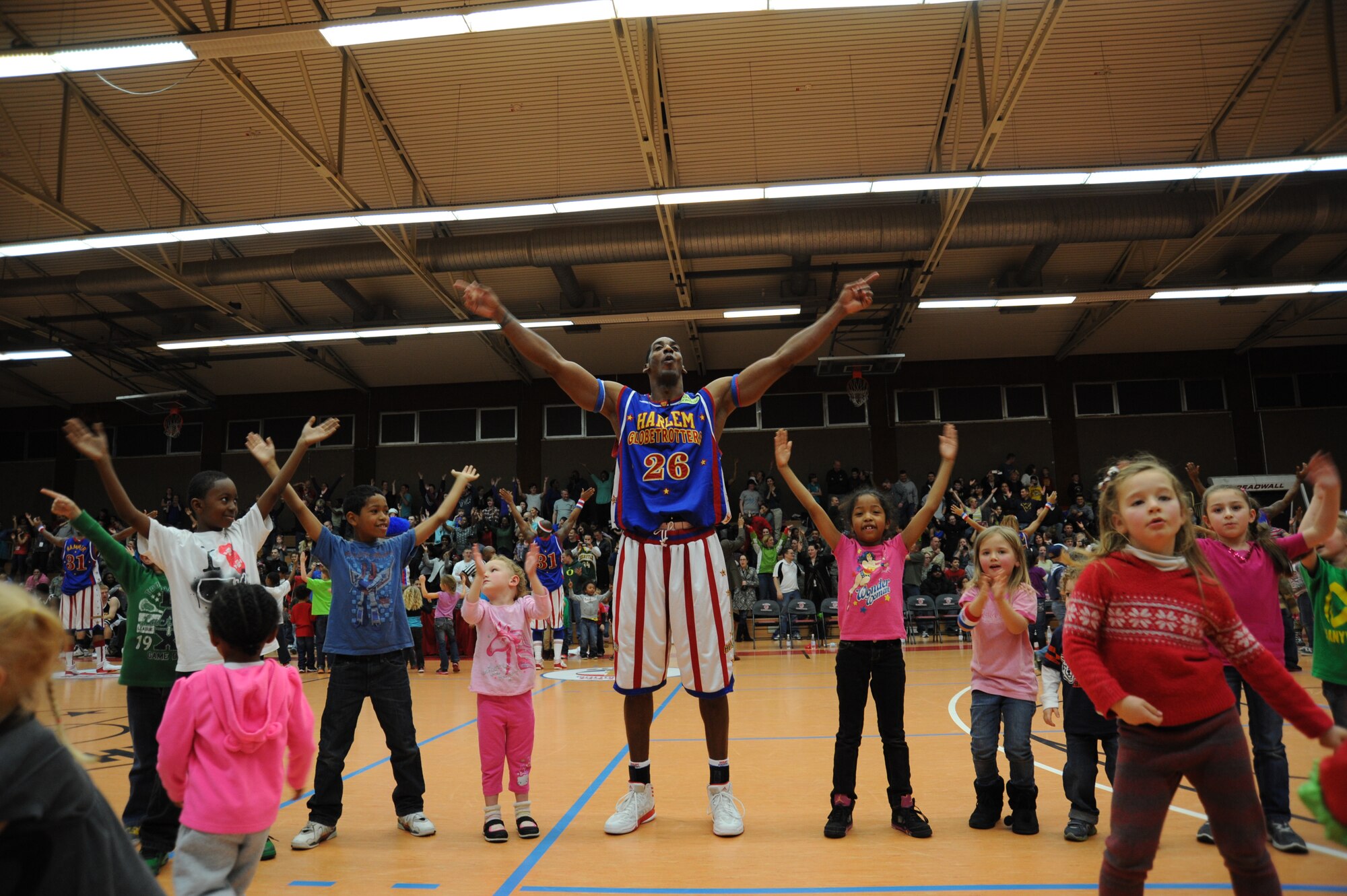 SPANGDAHLEM AIR BASE, Germany --- Hi-Lite, a Harlem Globetrotters basketball player, leads children and audience members in a dance during a complimentary game at the Skelton Memorial Fitness Center Dec. 4, 2013. The Globetrotters defeated the International Elite basketball team during the exhibition game 91-78. (U.S. Air Force photo by Airman 1st Class Dylan Nuckolls / Released)