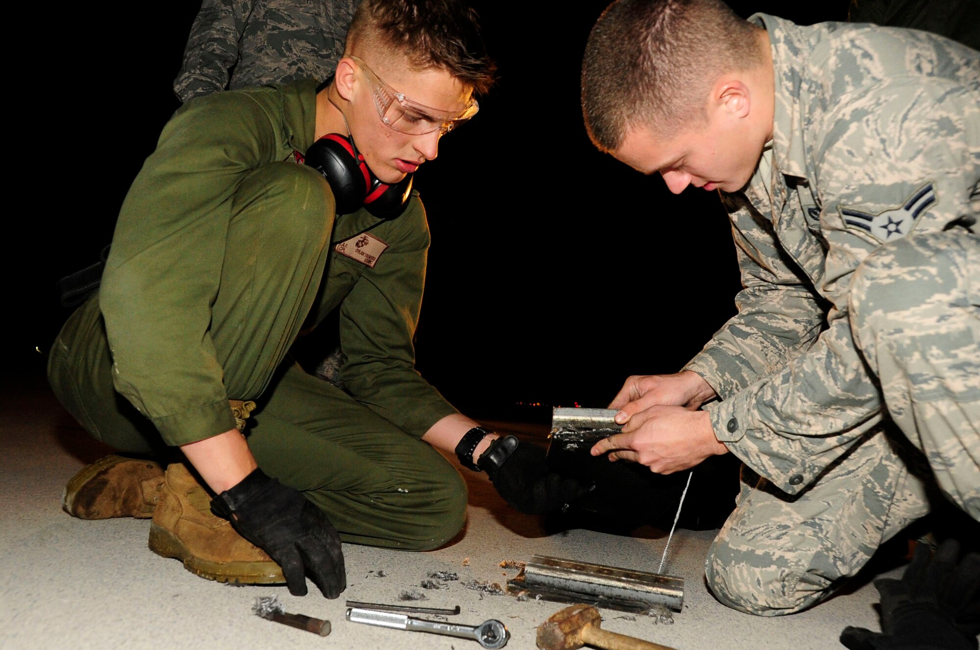U.S. Marine Corps  Lance Cpl. Dylan Travers works with Airman 1st Class Justin Clifford to ensure the tape is secured tightly to the aircraft arresting tape connector on Kadena Air Base, Japan, Dec. 6, 2013. Barrier maintenance technicians punch holes into the tape so the tape connector can connect onto it. Travers is assigned to the Marine Wing Headquarters Squadron as an expeditionary airfield technician from Northfork, Calif. Clifford from Wash., is assigned to the 18th Civil Engineer Squadron electrical power production technician. (U.S. Air Force photo by Staff Sgt. Darnell T. Cannady)    