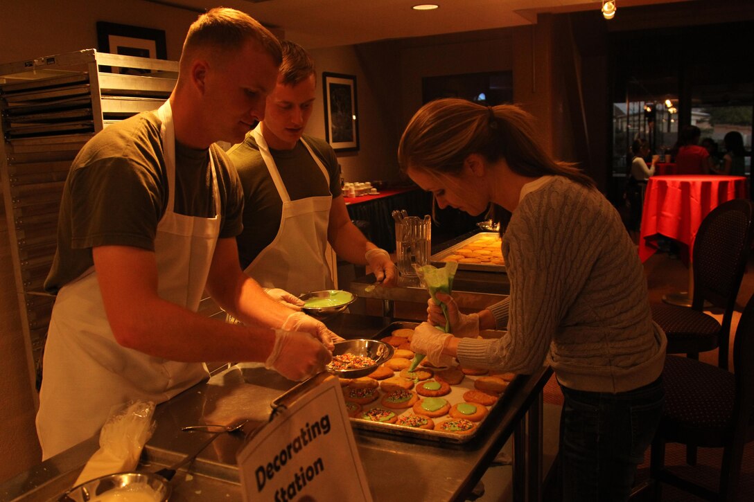 Michele Chamberlain, spouse of Capt. Travis Chamberlain, helps two Marines with the Marine Corps Communication-electronics school, decorate sugar cookies at the Combat Center's Officer's Club in support of the Treats for Troops event Dec. 3, 2013.